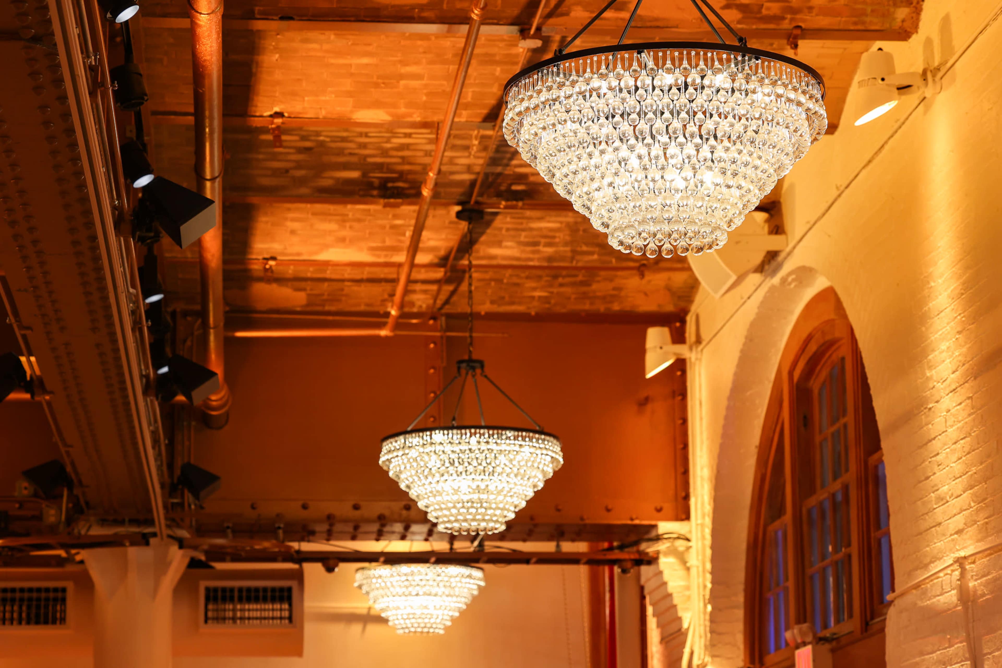Three large crystal chandeliers hang from the ceiling in a well-lit venue.