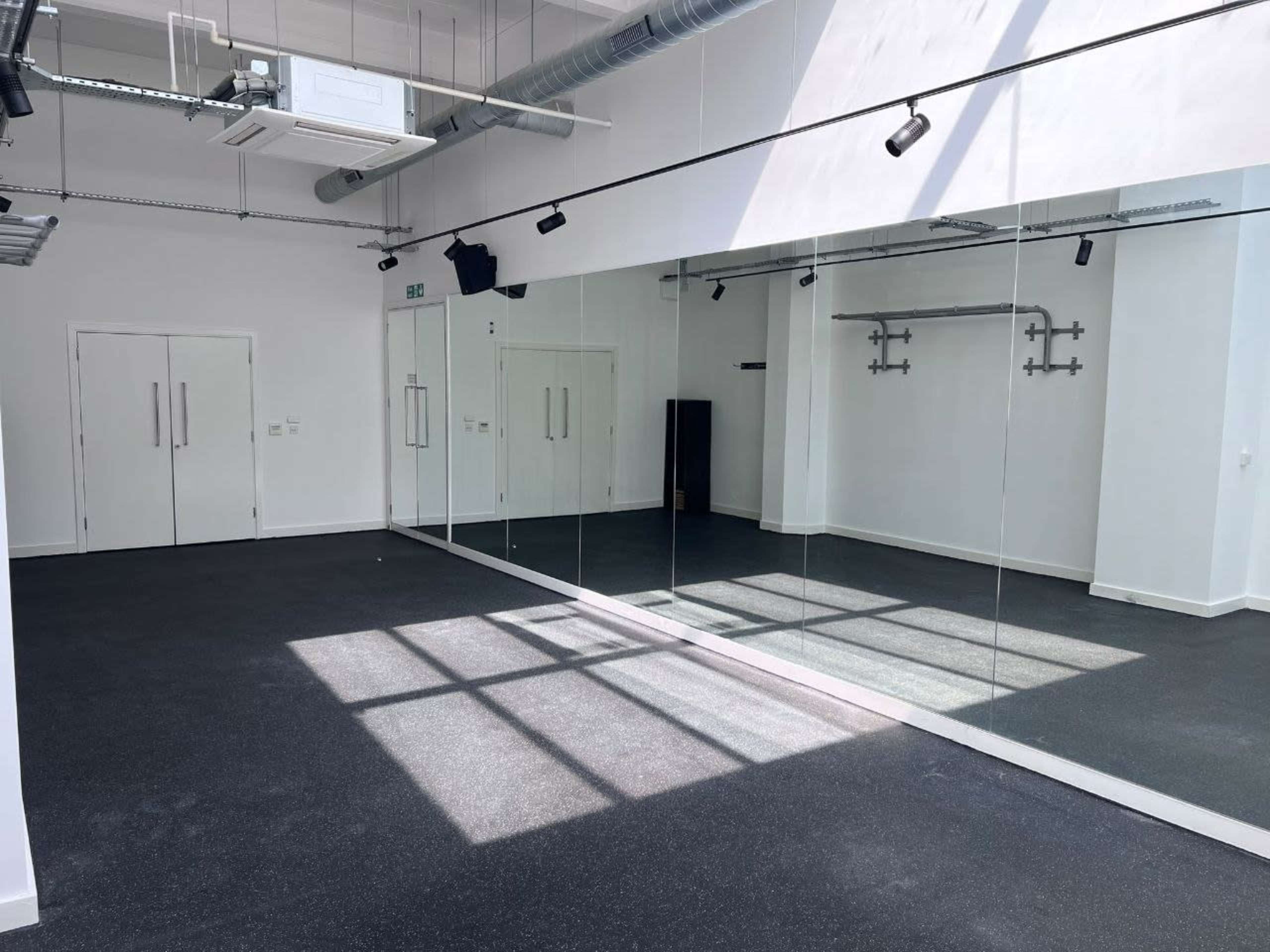 A spacious room with a dark floor and large mirrors reflecting light from the windows above.
