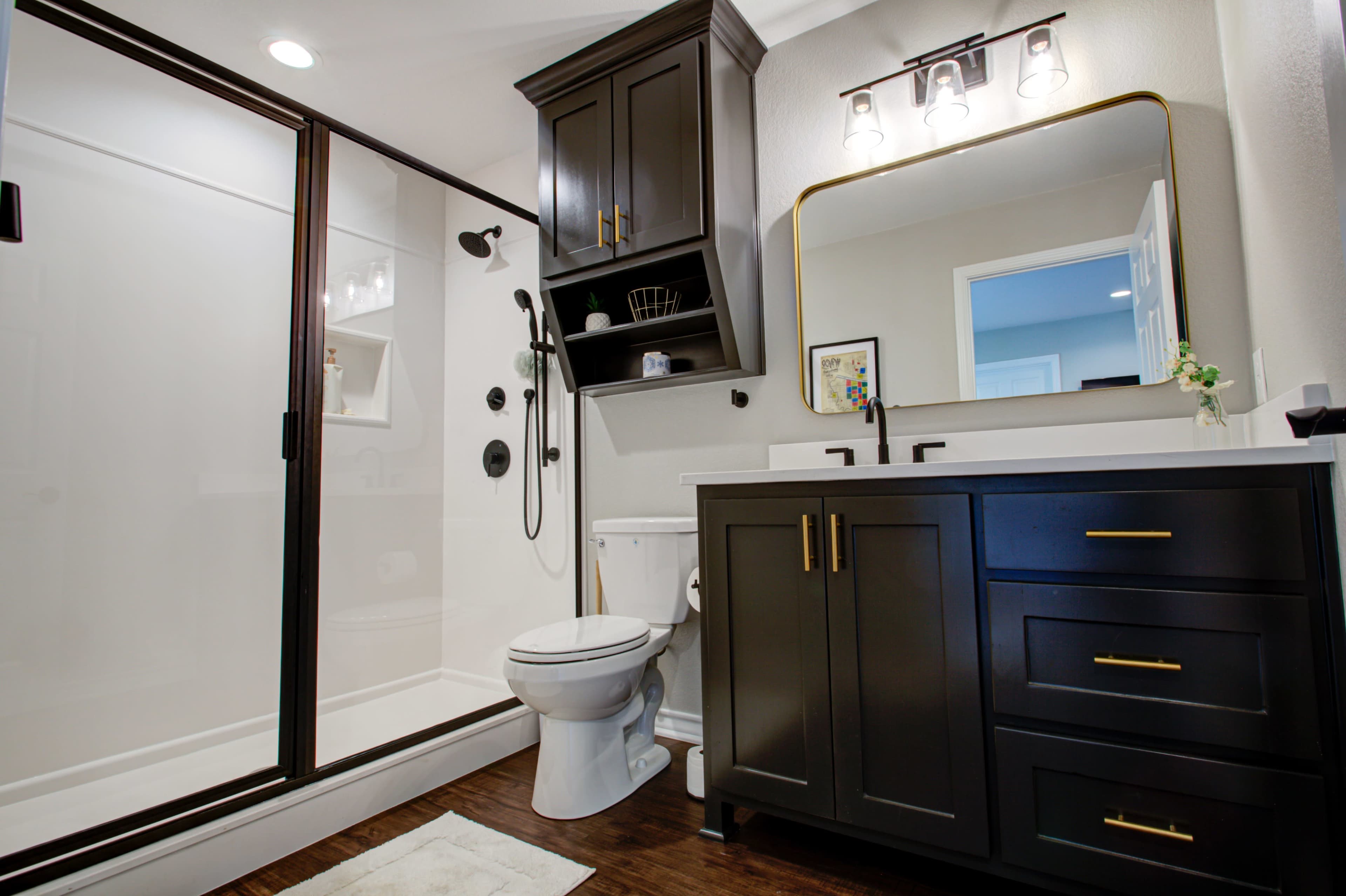 A modern bathroom featuring a glass shower, dark cabinetry, a double sink vanity, and neutral-colored walls.