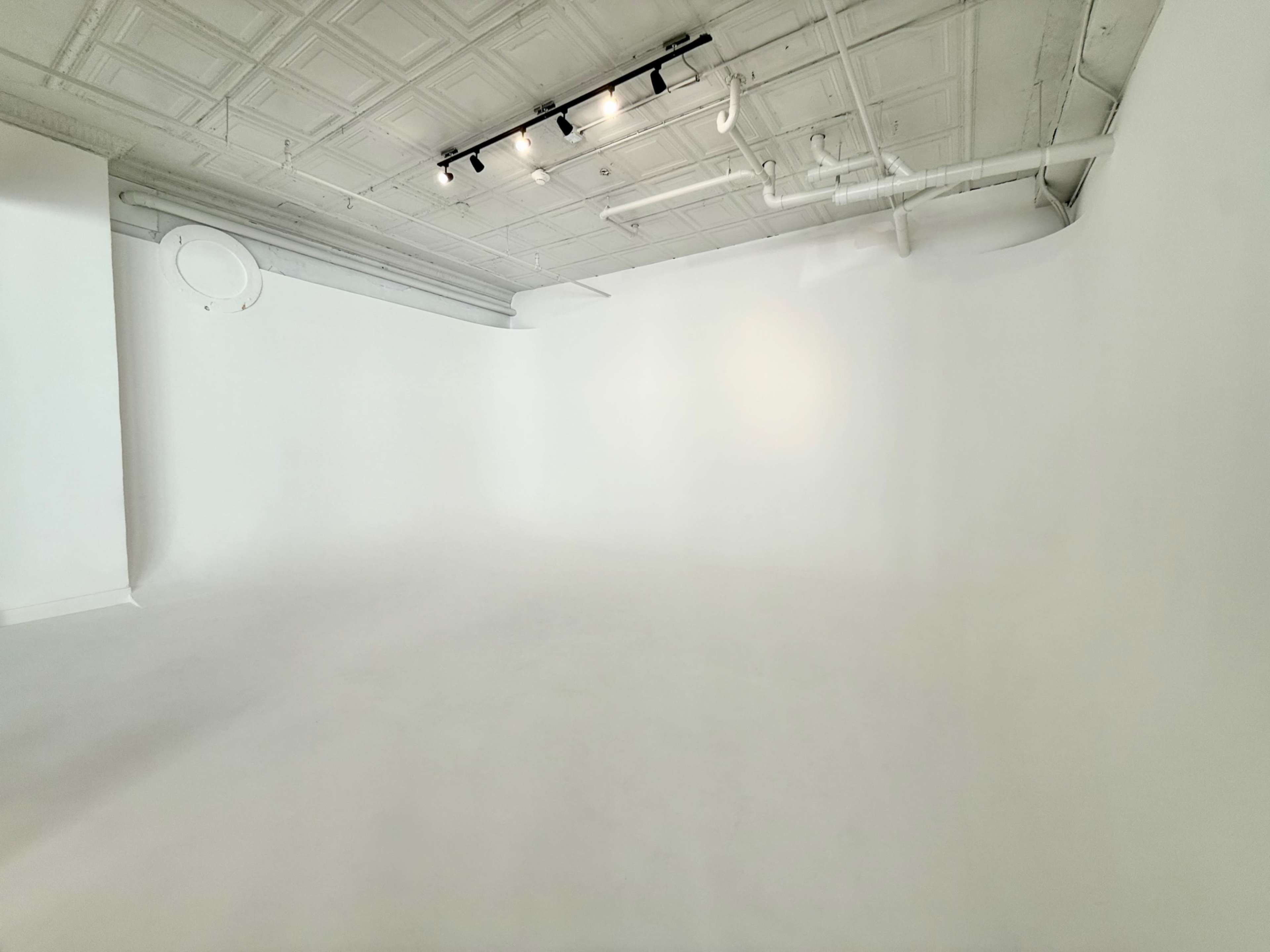 The image shows a spacious, empty studio with white walls and a seamless white floor.