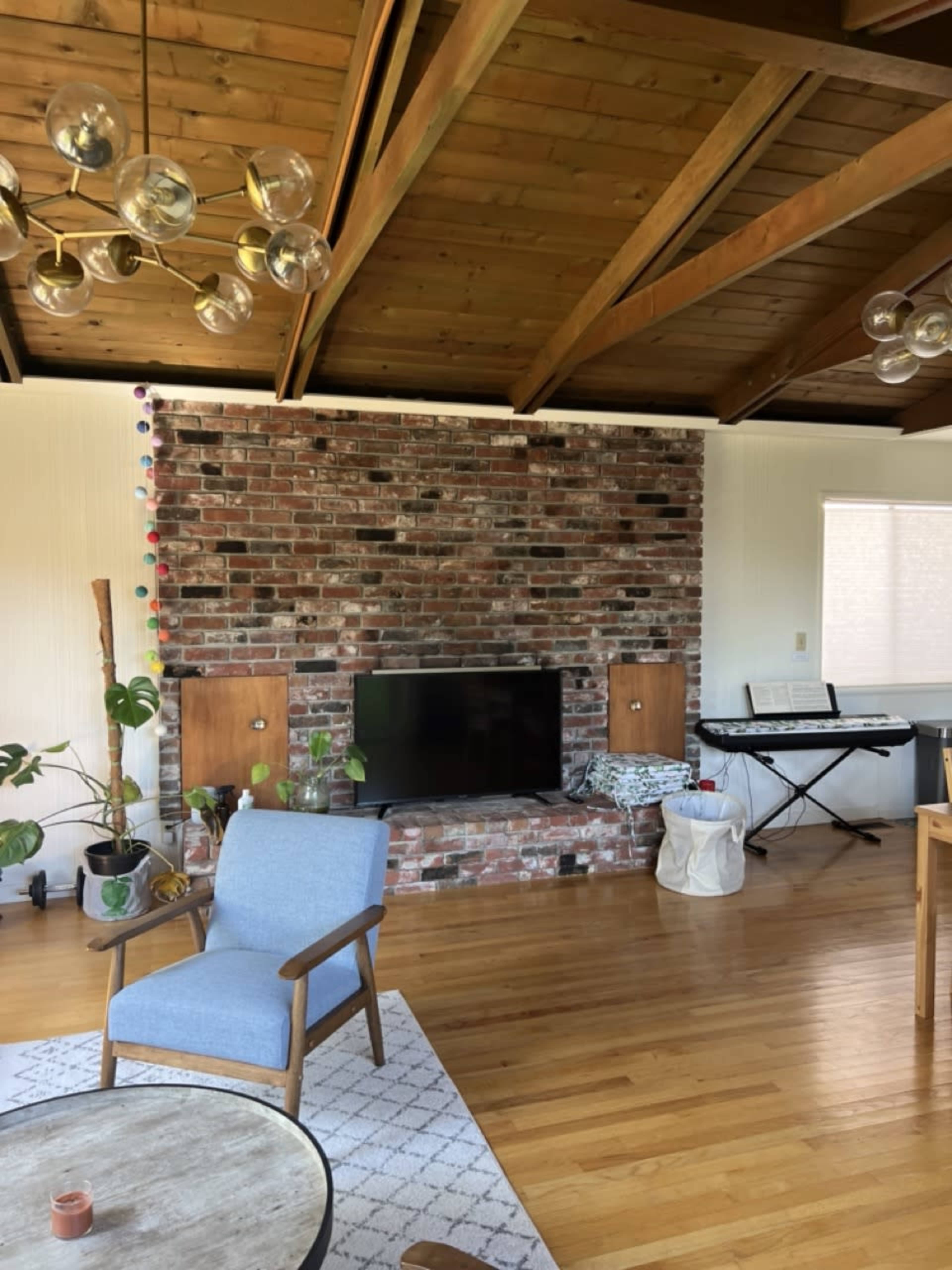 A living room with a brick accent wall, a television, a potted plant, a light blue armchair, and a keyboard in the background.