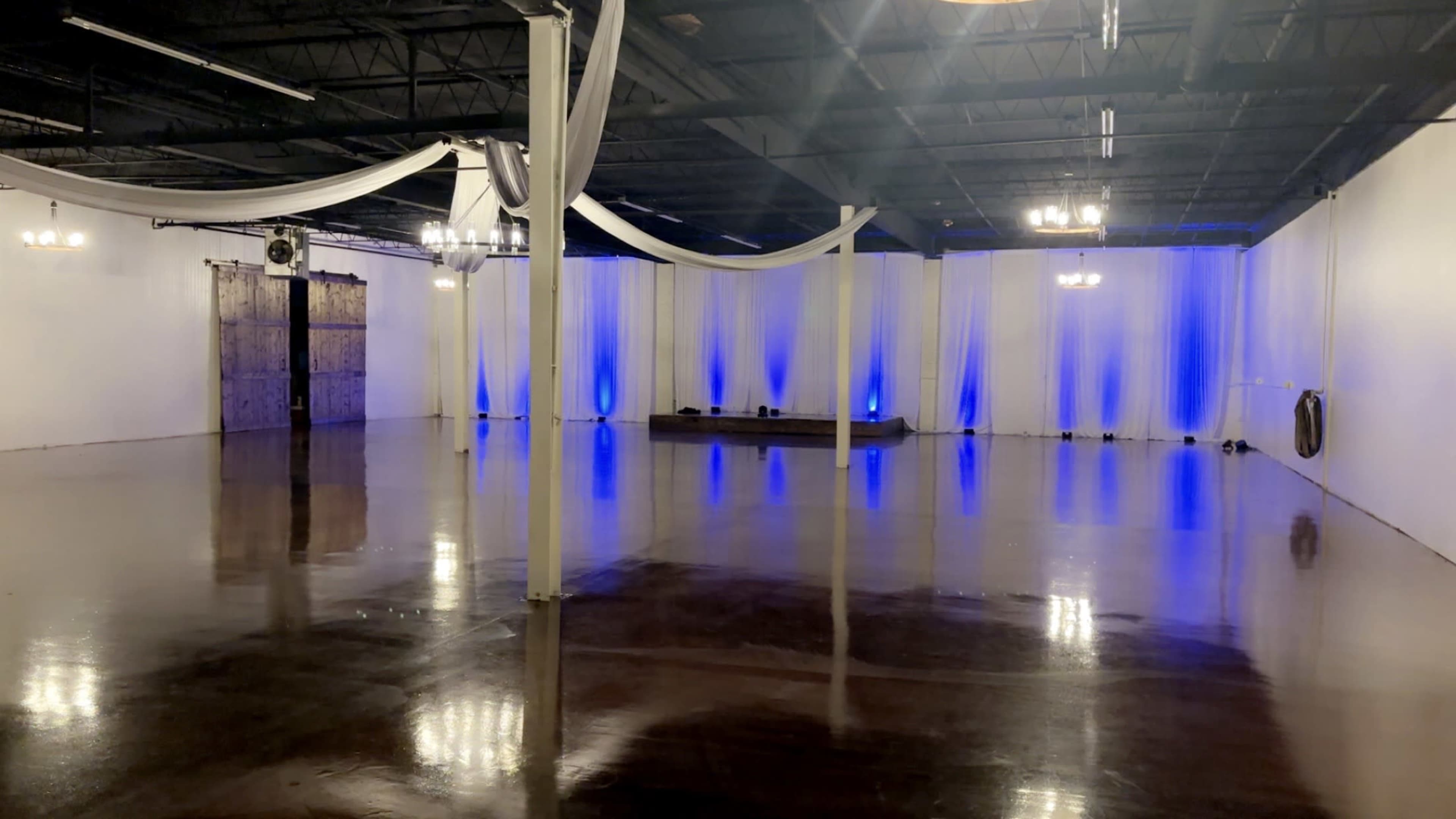 The image shows a spacious indoor venue with polished floors, white draped curtains, and blue lighting along the walls.