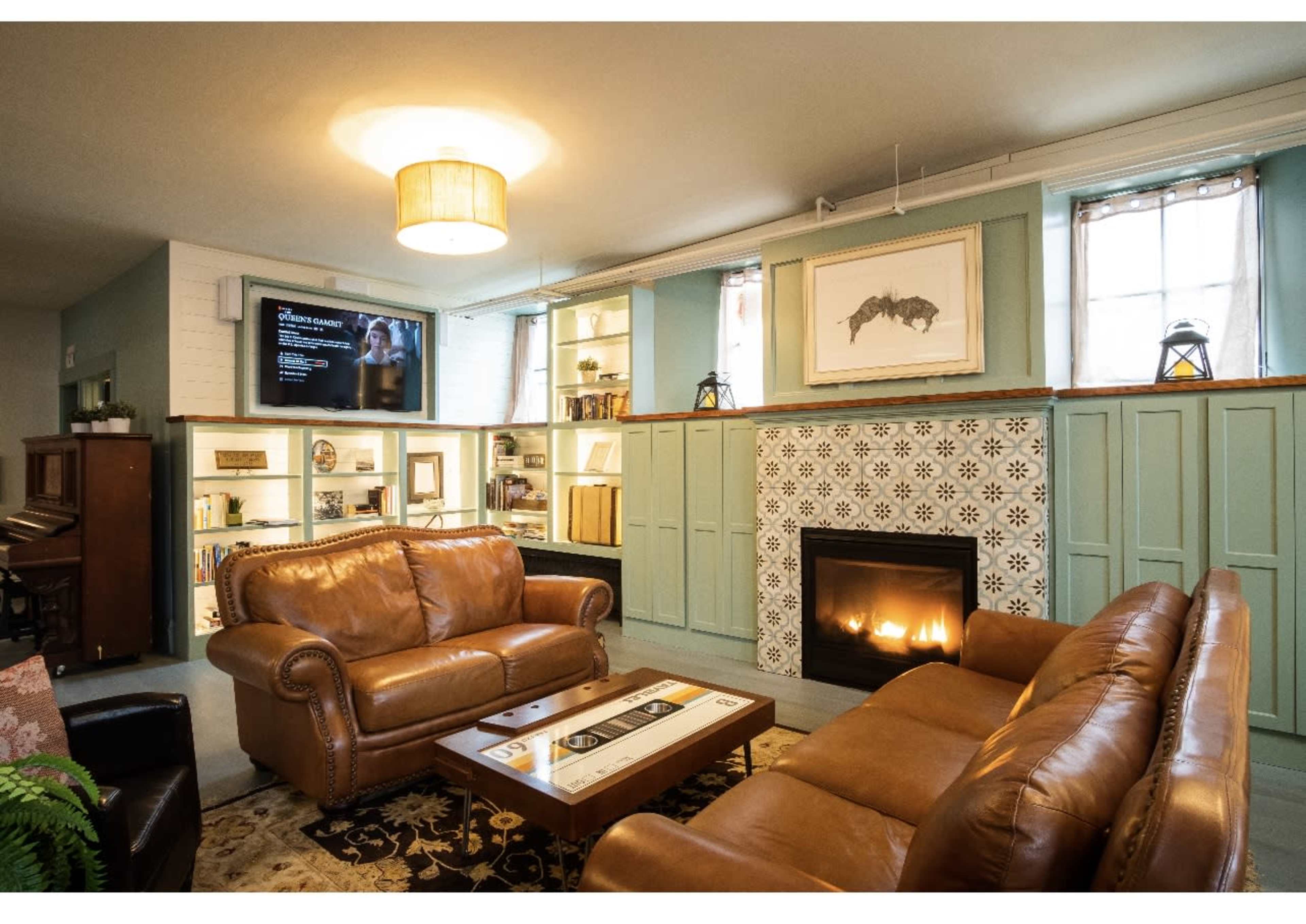 The living room features two brown leather sofas facing a tiled fireplace, with built-in shelves displaying books and decorative items.