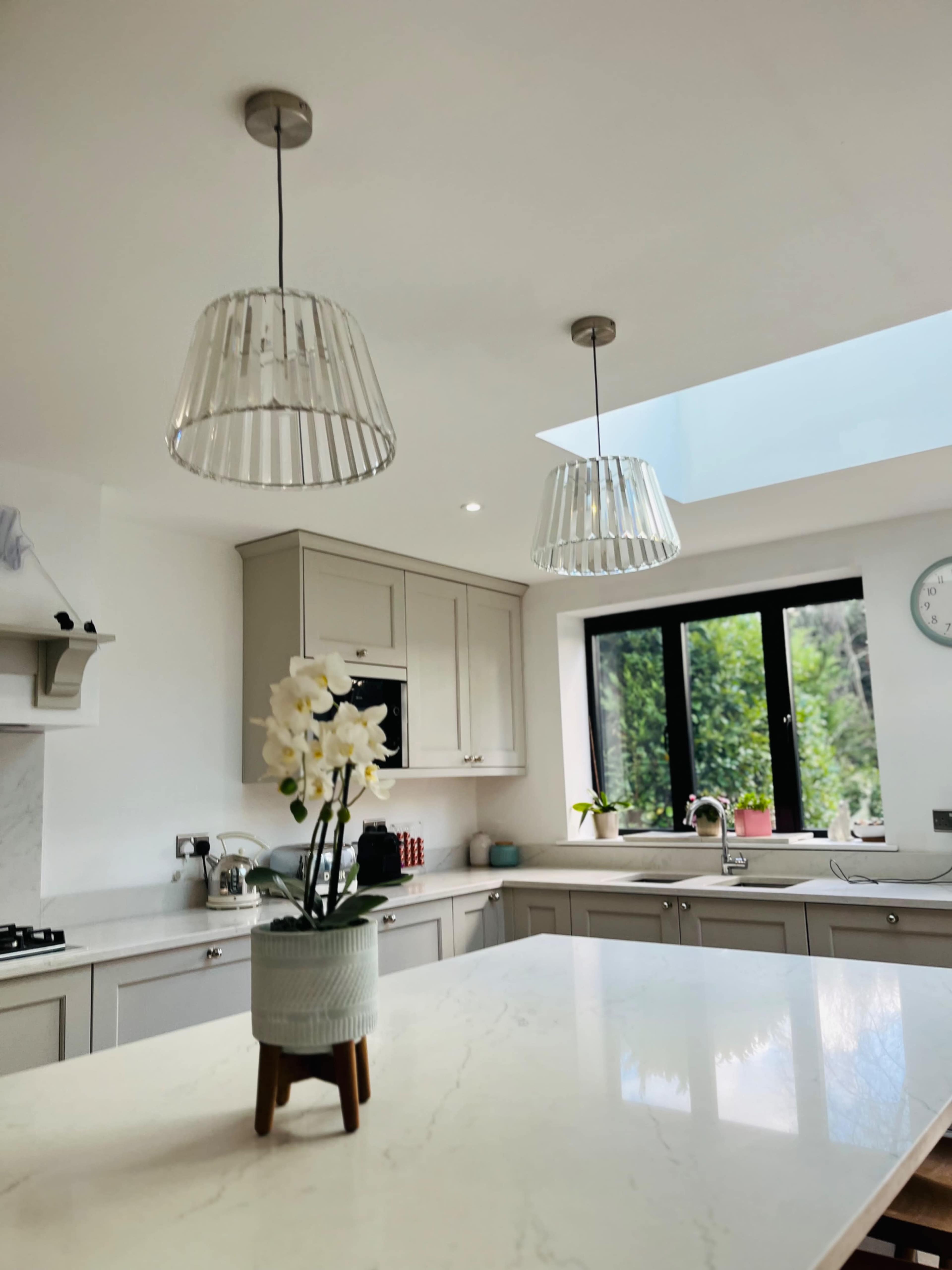 The image shows a modern kitchen with light gray cabinetry, a marble countertop, and two pendant lights hanging from the ceiling.