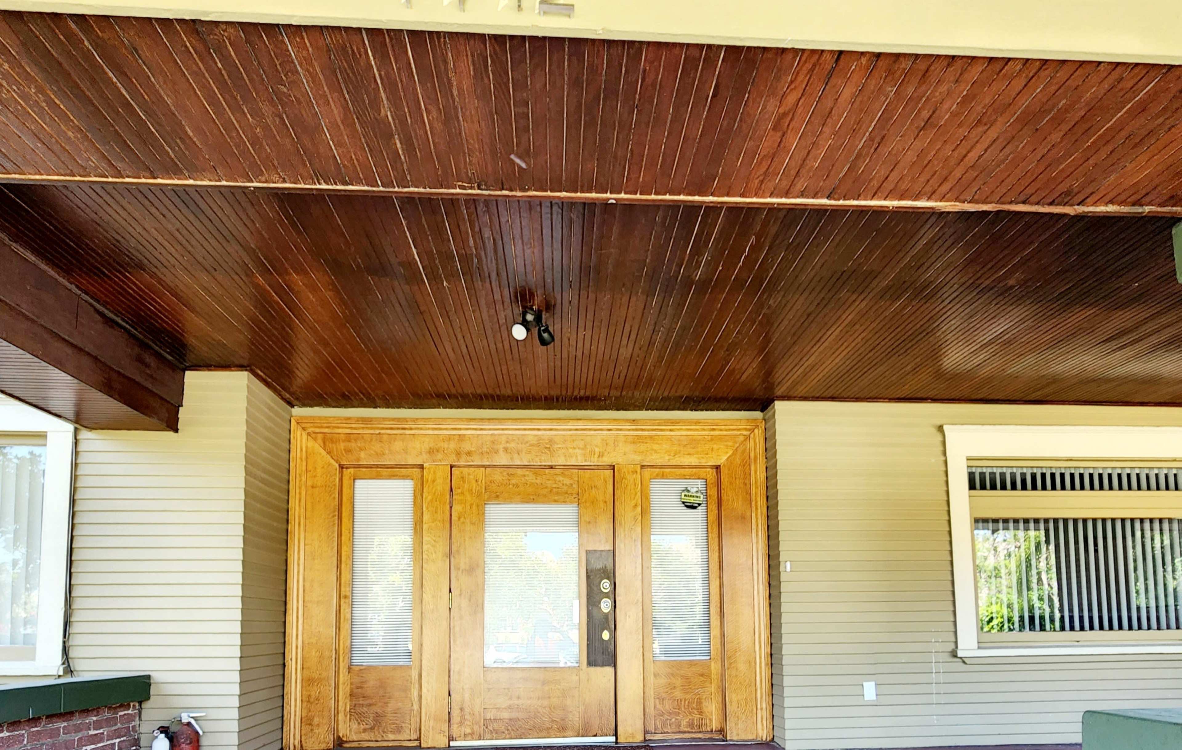 A porch area featuring a wooden ceiling and a set of double wooden doors.