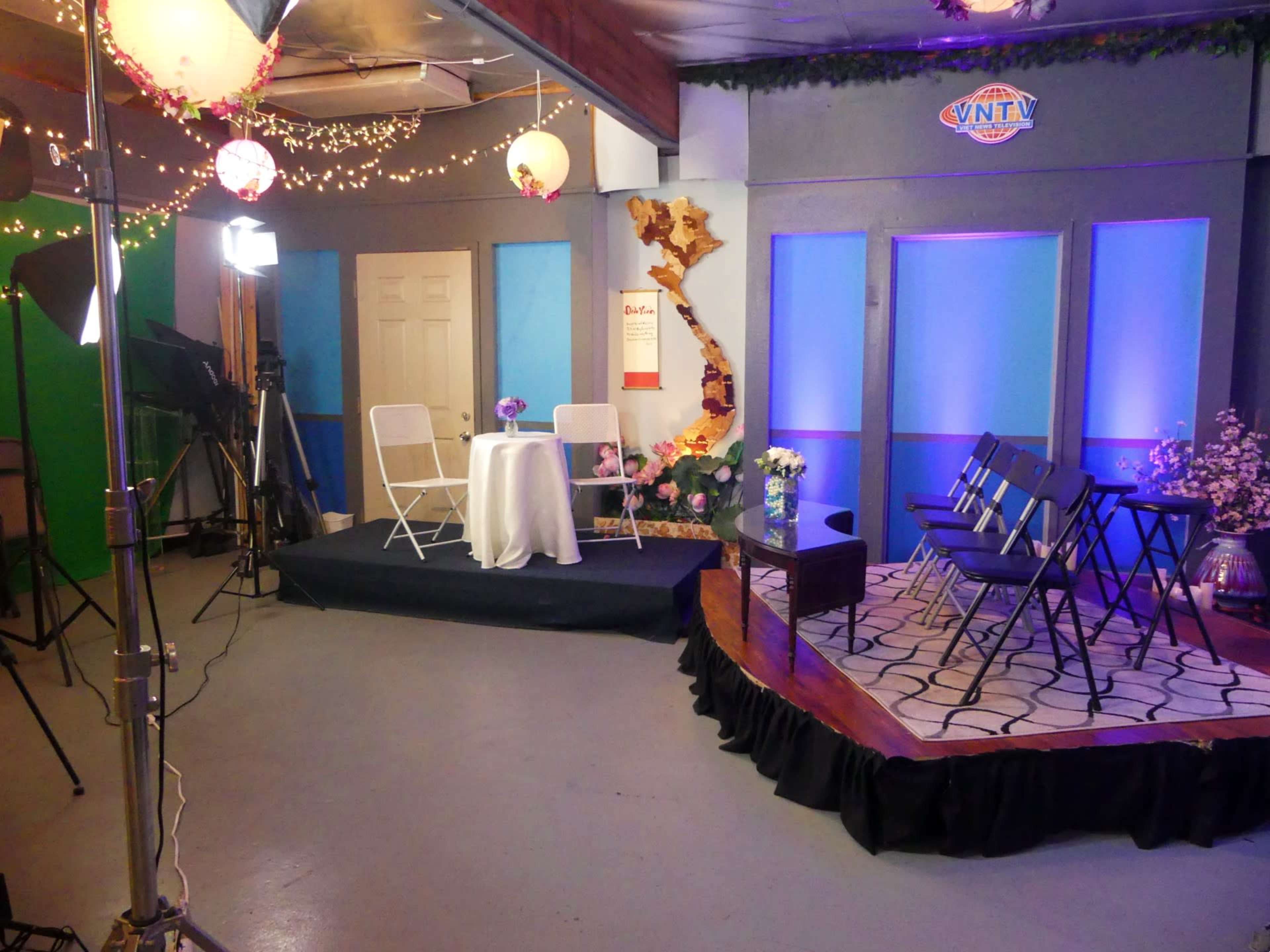 A television studio setup with chairs arranged in a semi-circle around a small table, decorated with flowers and soft lighting.