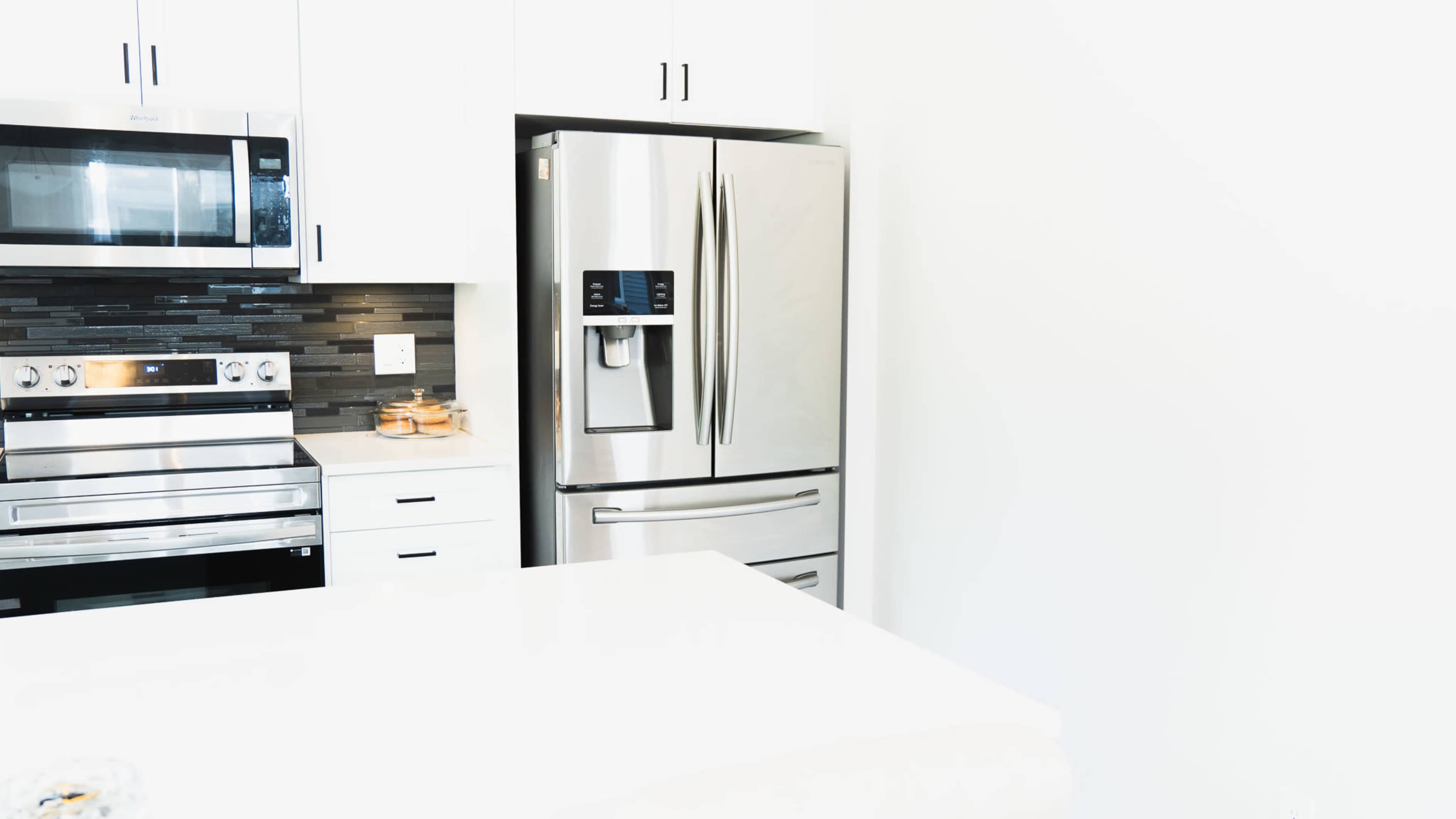 A modern kitchen features stainless steel appliances, including a refrigerator, an oven, and a microwave, set against a light-colored wall and countertop.