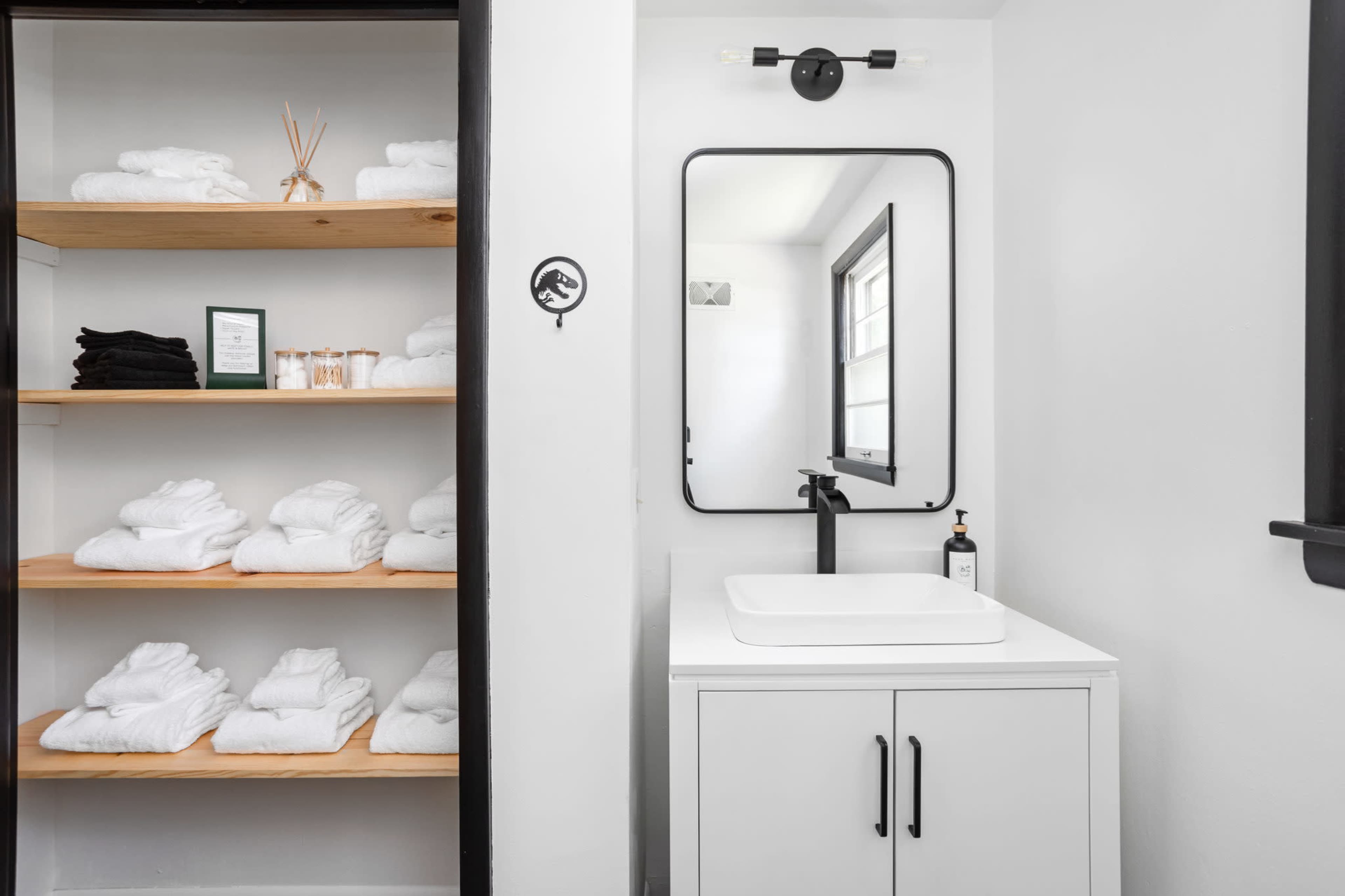 A modern bathroom featuring neatly arranged towels on wooden shelves and a vanity with a square sink and a mirror.