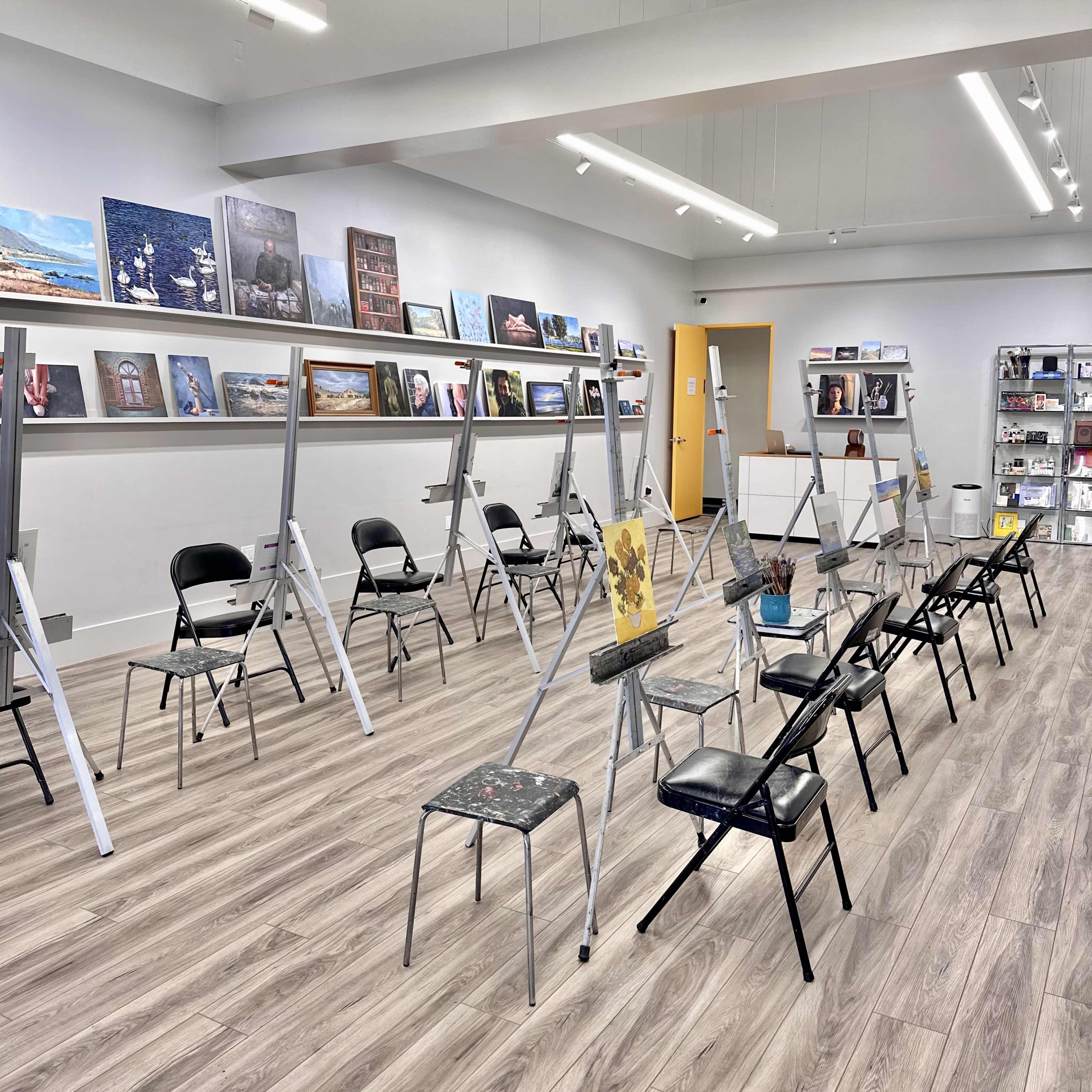 A spacious art studio with easels set up in rows, surrounded by framed artworks on the walls.
