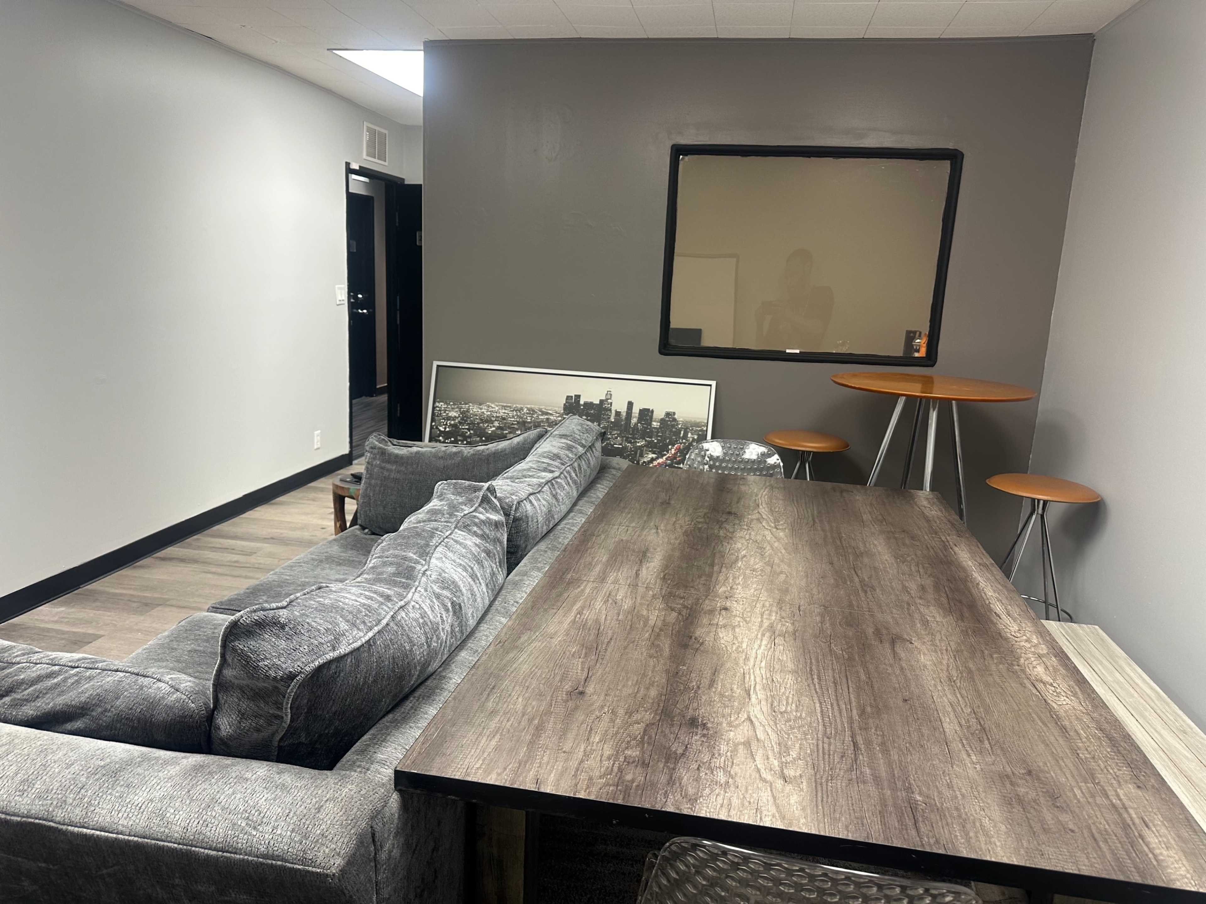 A modern room with a gray wall, a wooden table, a couch, and three stools around the table.