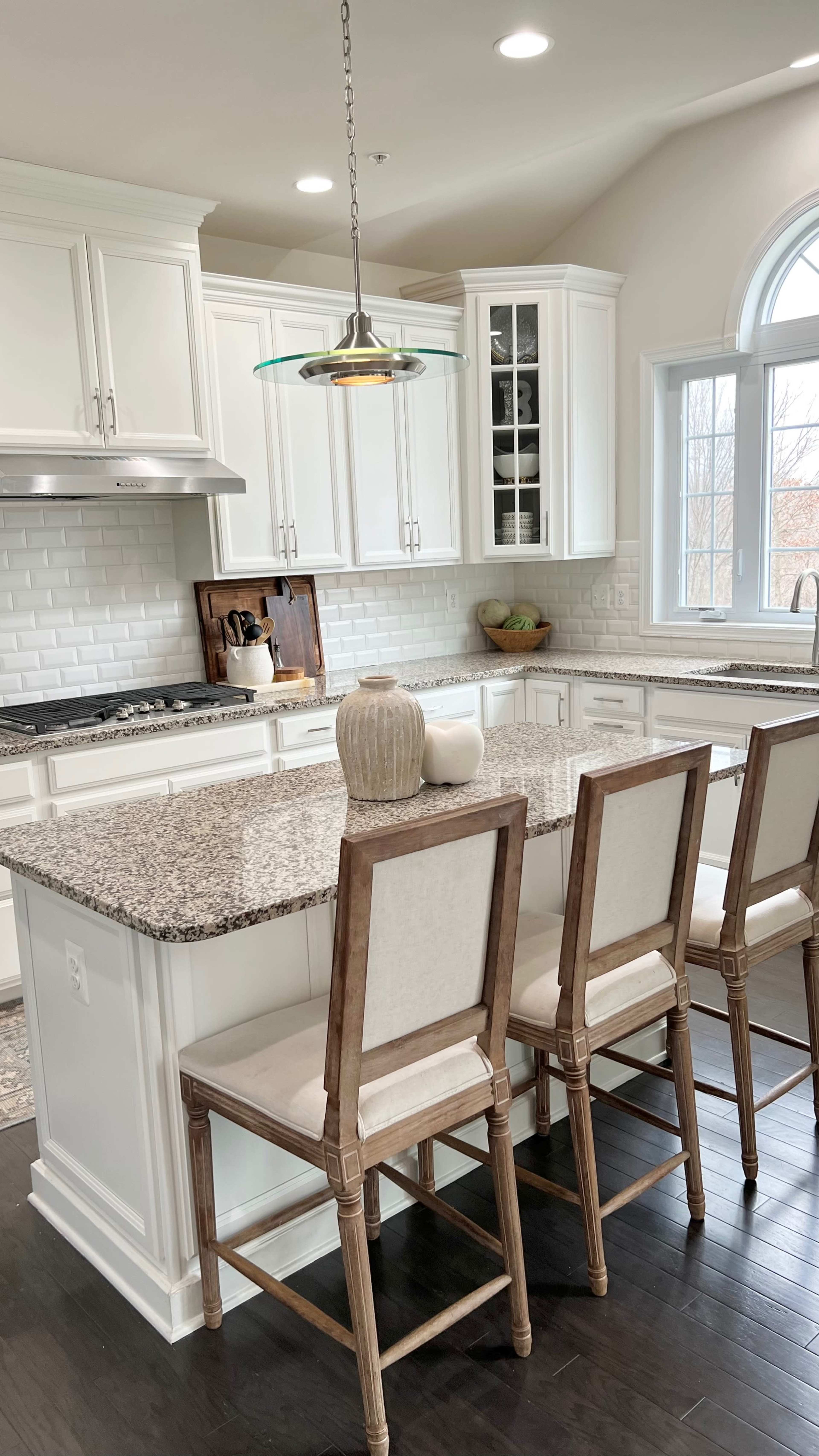 A modern kitchen features white cabinetry, a large granite island with seating, and a pendant light above.