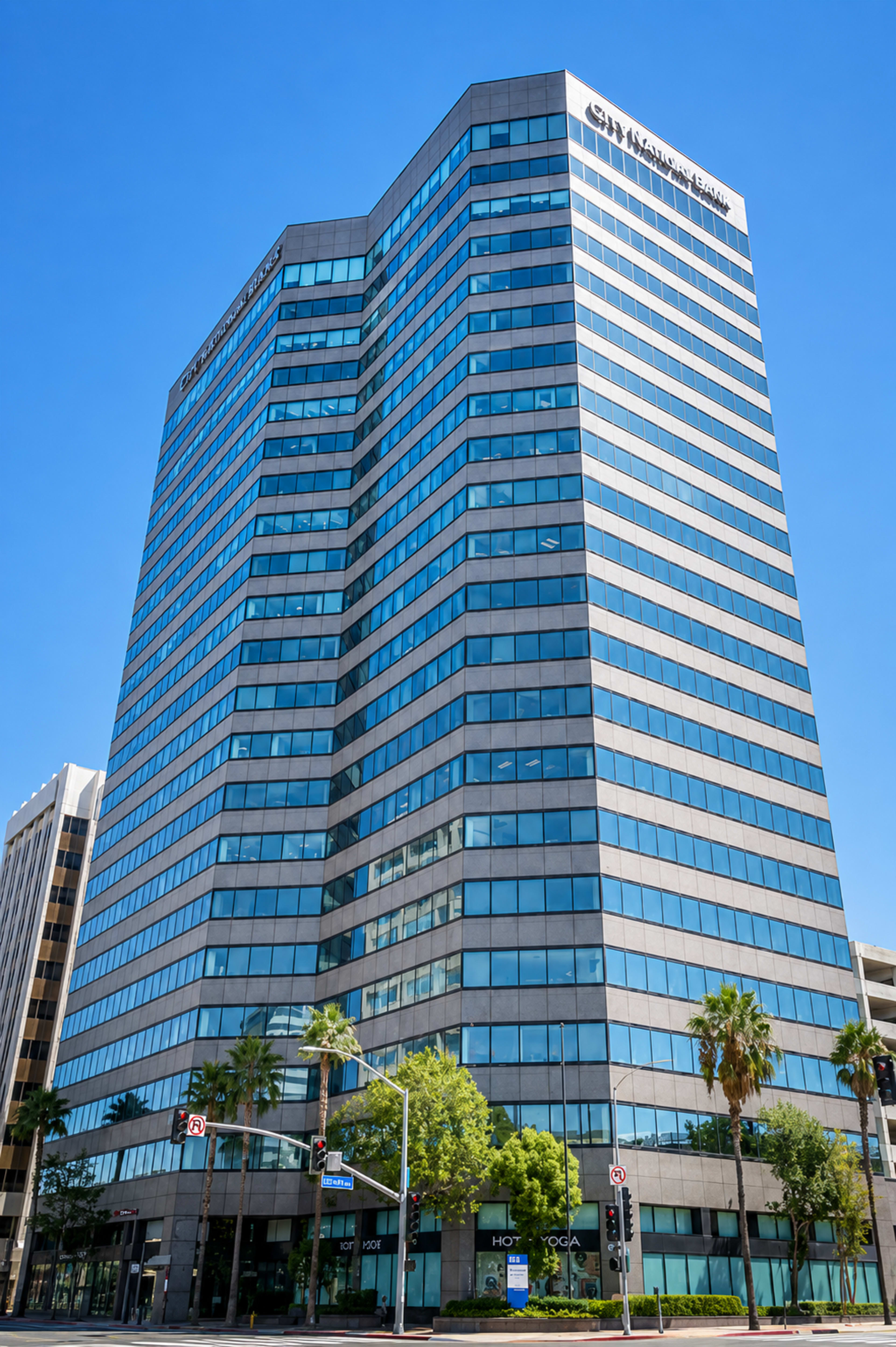 A tall, modern office building with glass windows and palm trees in the foreground.