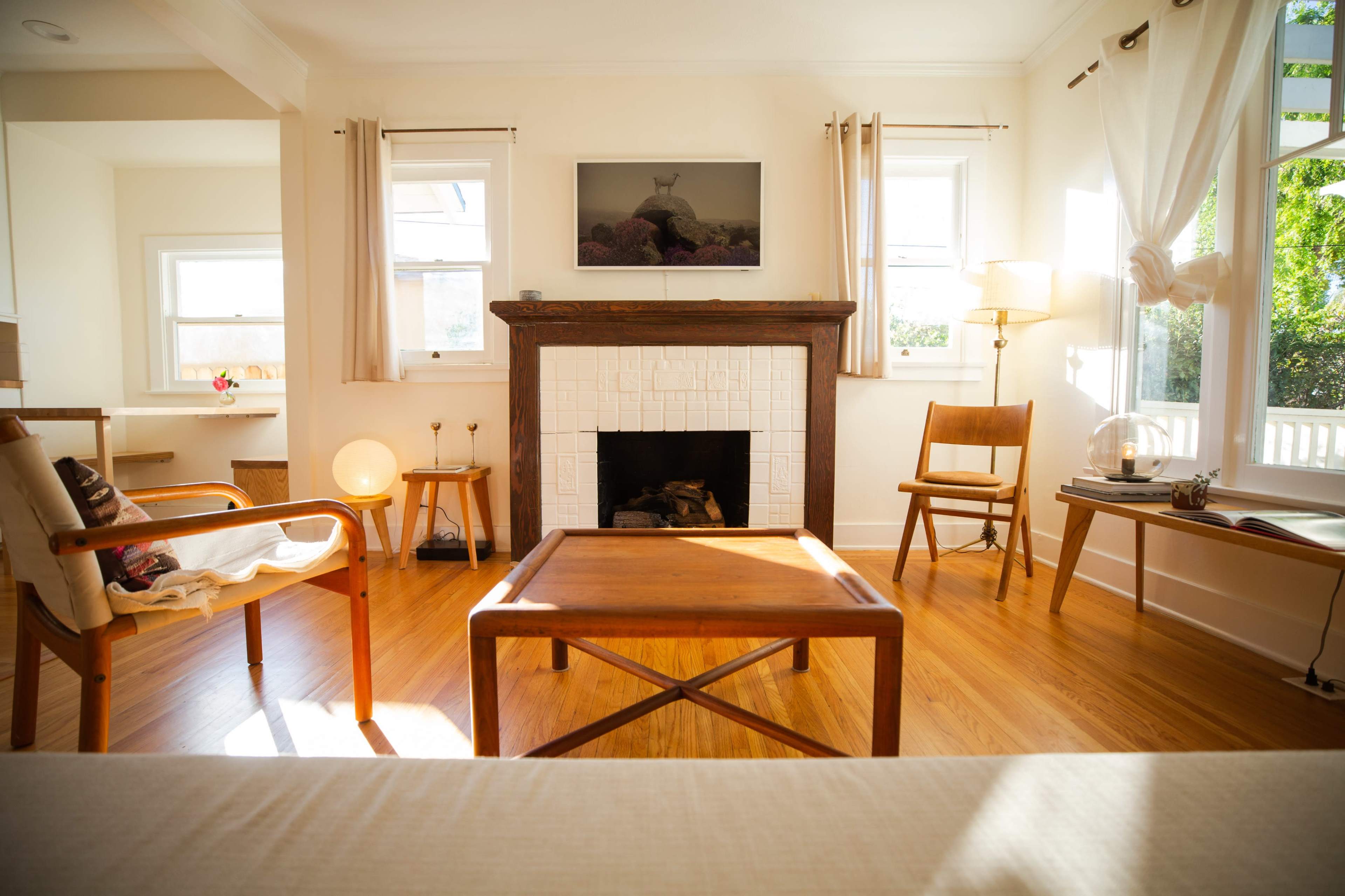 The room features a wooden coffee table at the center, surrounded by chairs and a fireplace, with large windows allowing natural light to fill the space.