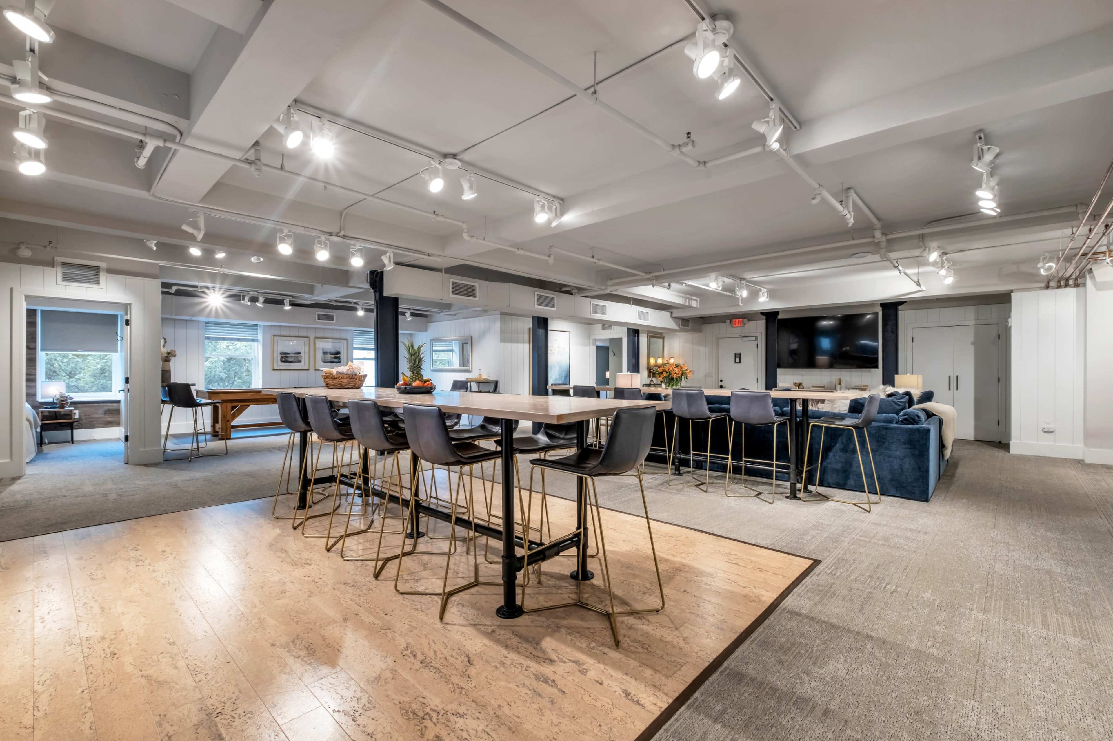 The image shows a modern, open-concept multi-functional space with a dining area, seating area, and large windows.