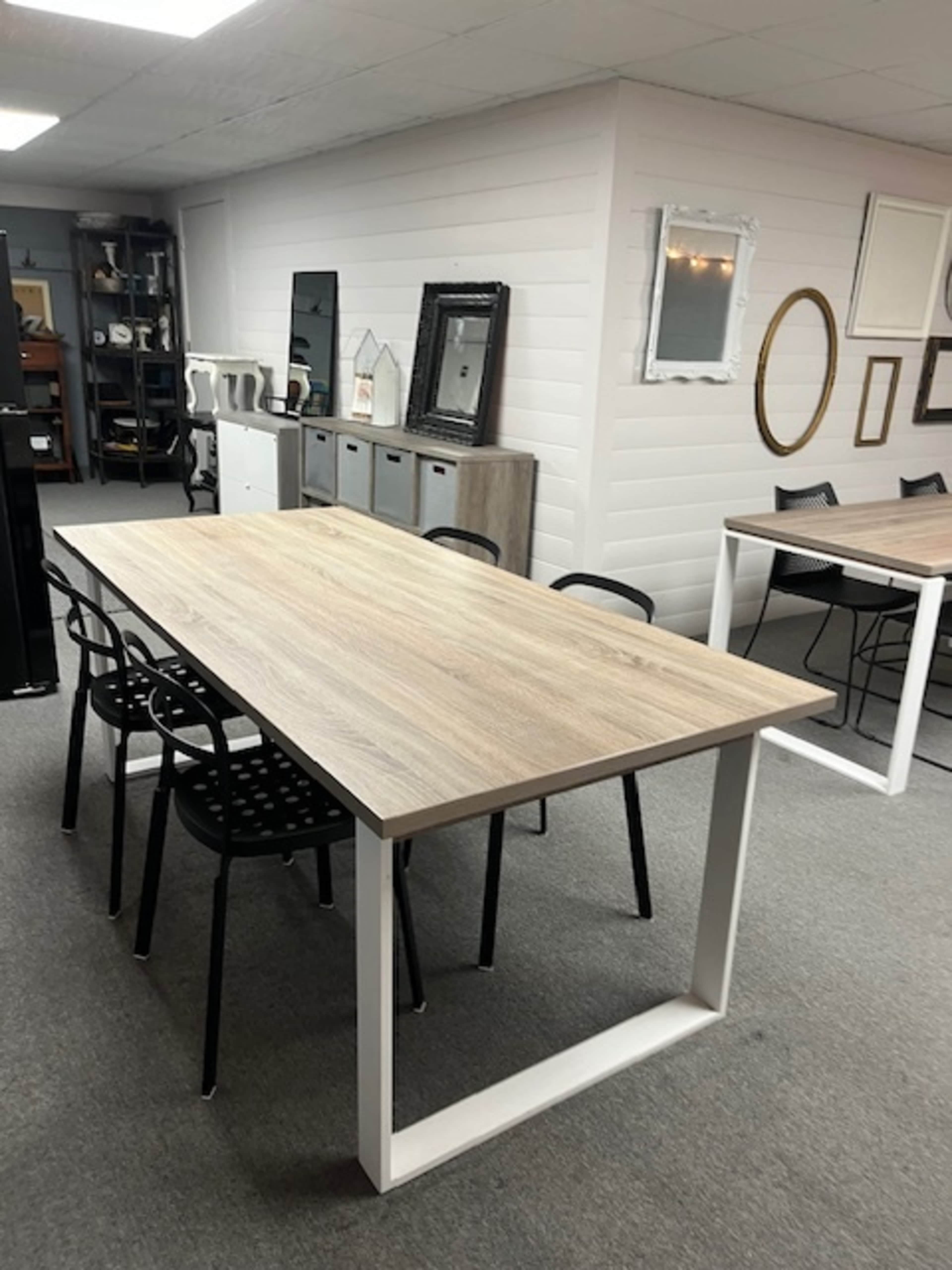 A large, wooden dining table with a light finish is surrounded by black chairs in a showroom featuring various home decor items.