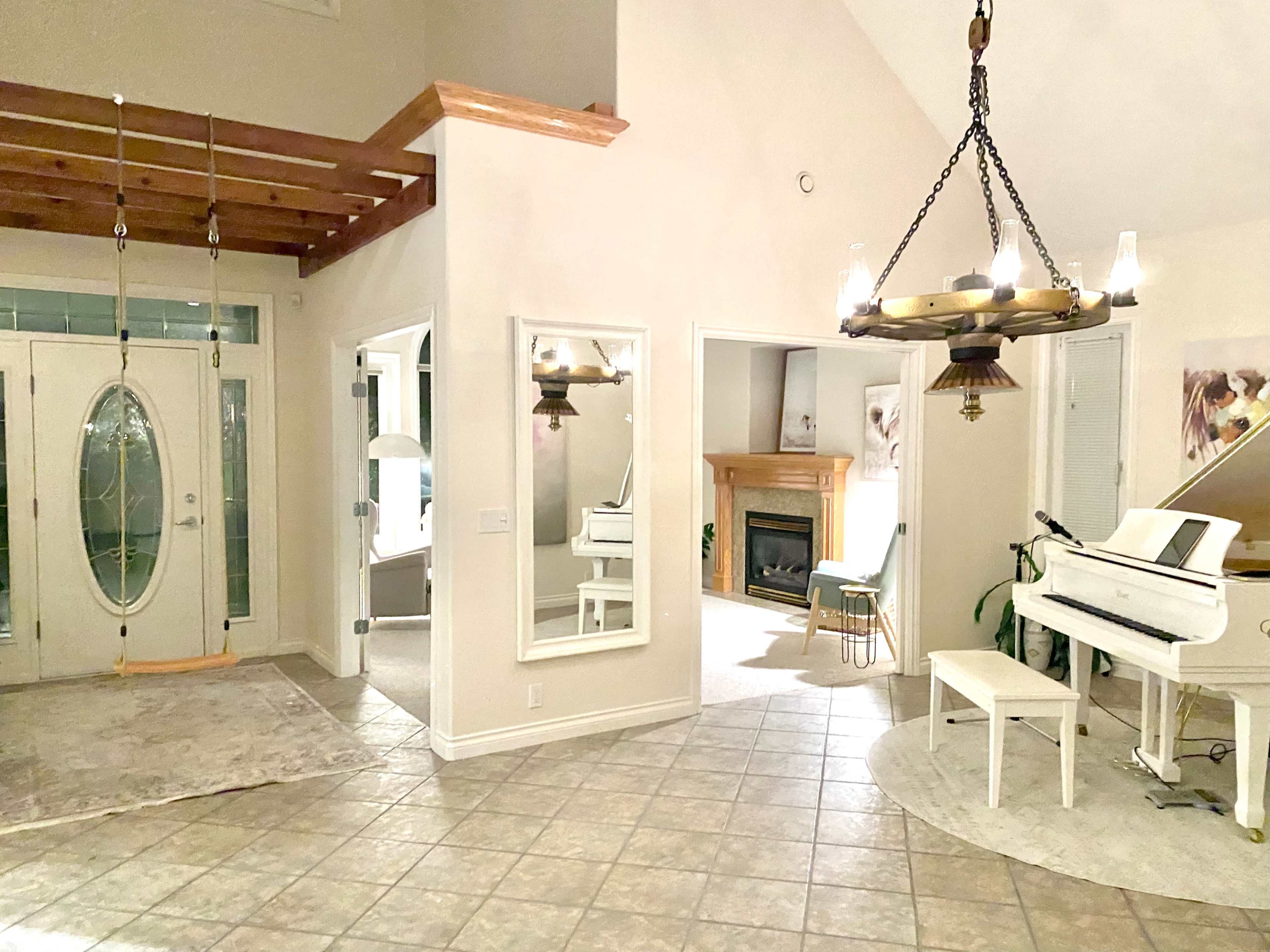A spacious entryway with a white piano, a swing hanging from the ceiling, and large mirrors reflecting a well-lit interior.