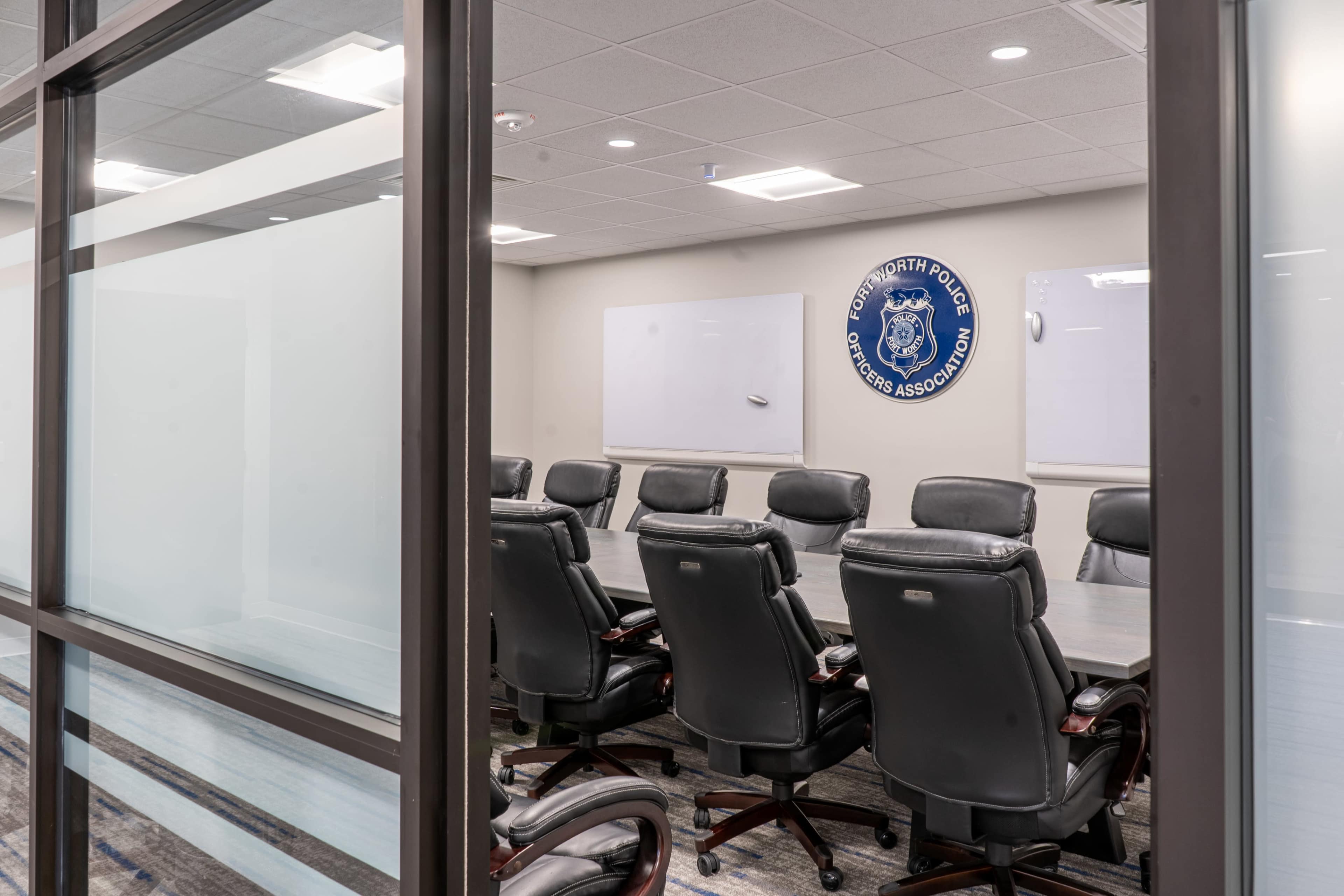 A meeting room with a long table surrounded by ergonomic chairs and a wall displaying a police association logo.