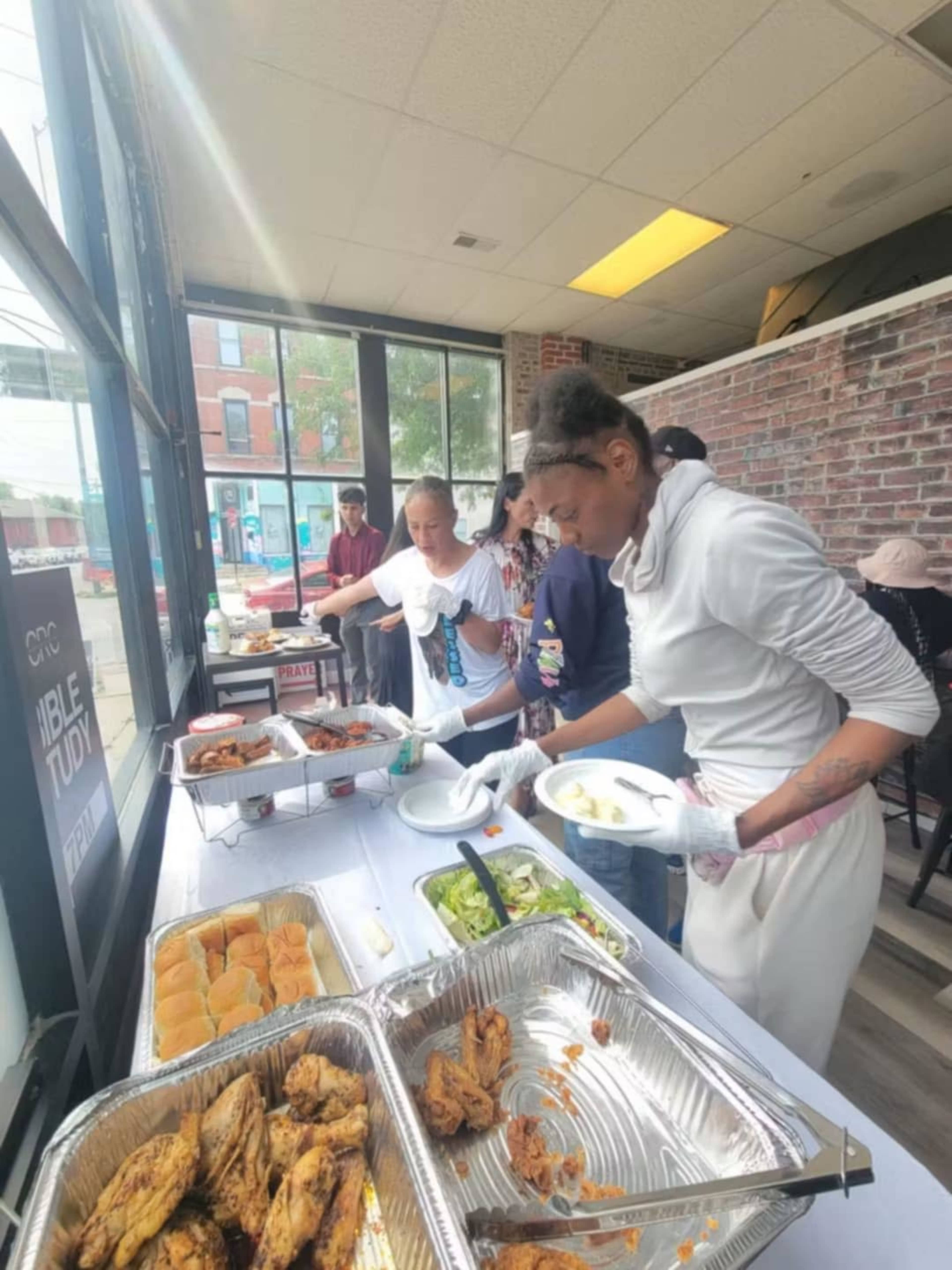 A group of people is serving food from a buffet table in a brightly lit restaurant setting.