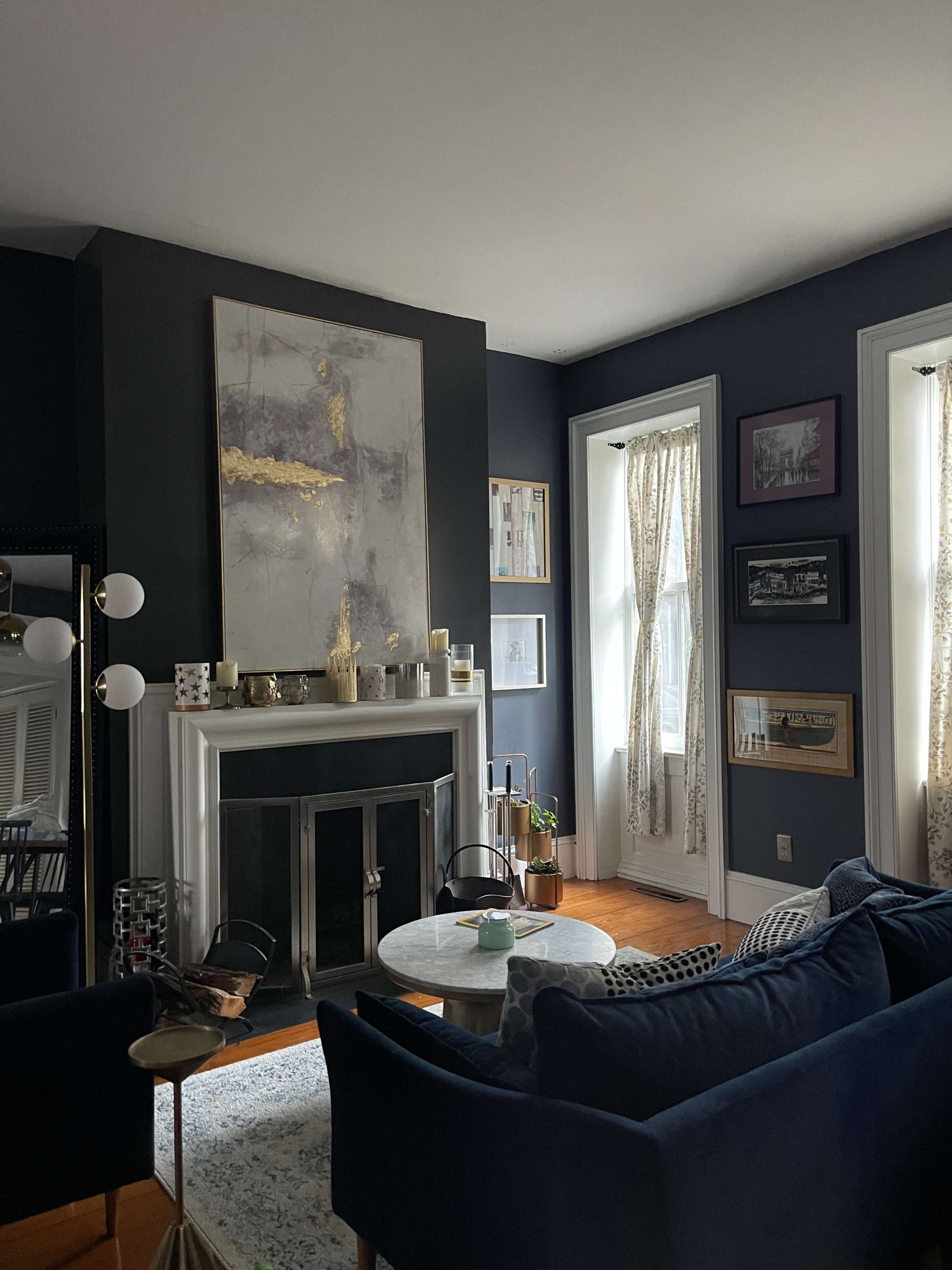 The living room features a dark blue wall, a large abstract painting above the fireplace, and a mix of framed artwork on the walls.