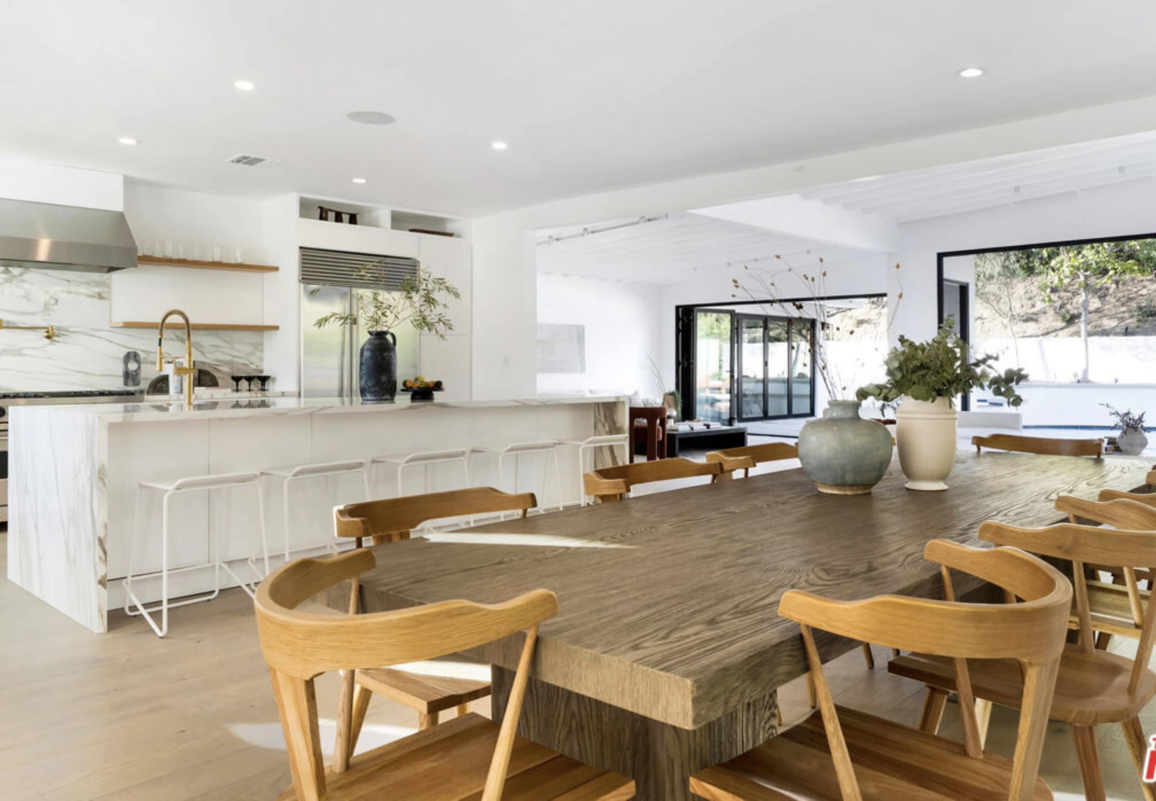 A spacious dining area features a large wooden table surrounded by chairs, with a modern kitchen visible in the background.