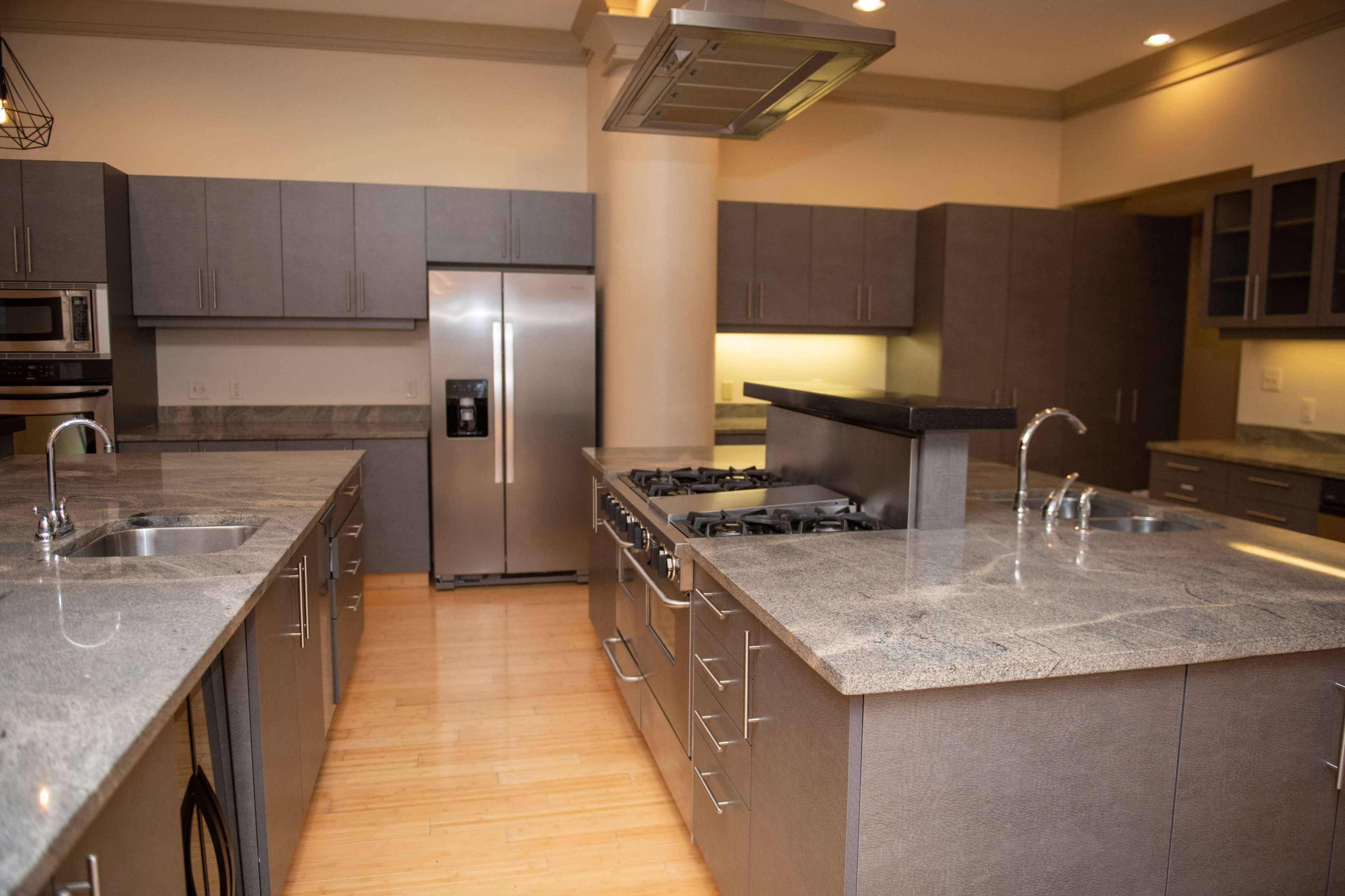 The image shows a modern kitchen with stainless steel appliances, gray cabinetry, and large countertops.