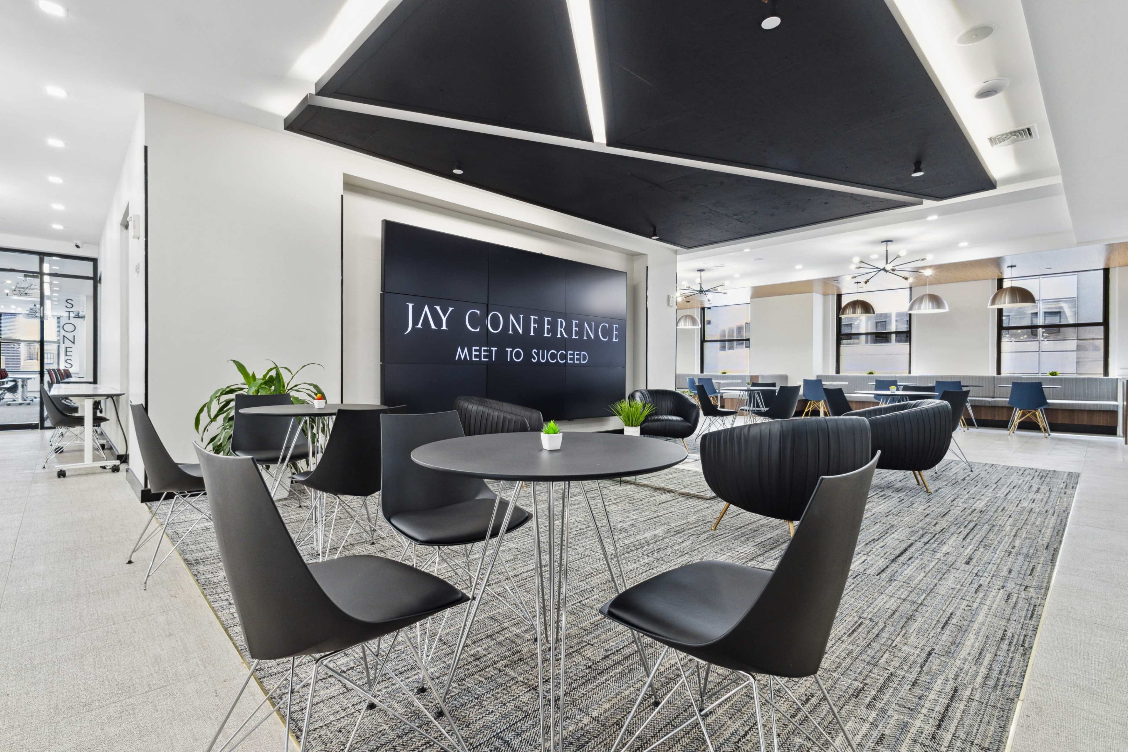 A modern conference room featuring sleek black chairs, a round table, and a large wall sign that reads "JAY CONFERENCE MEET TO SUCCEED."