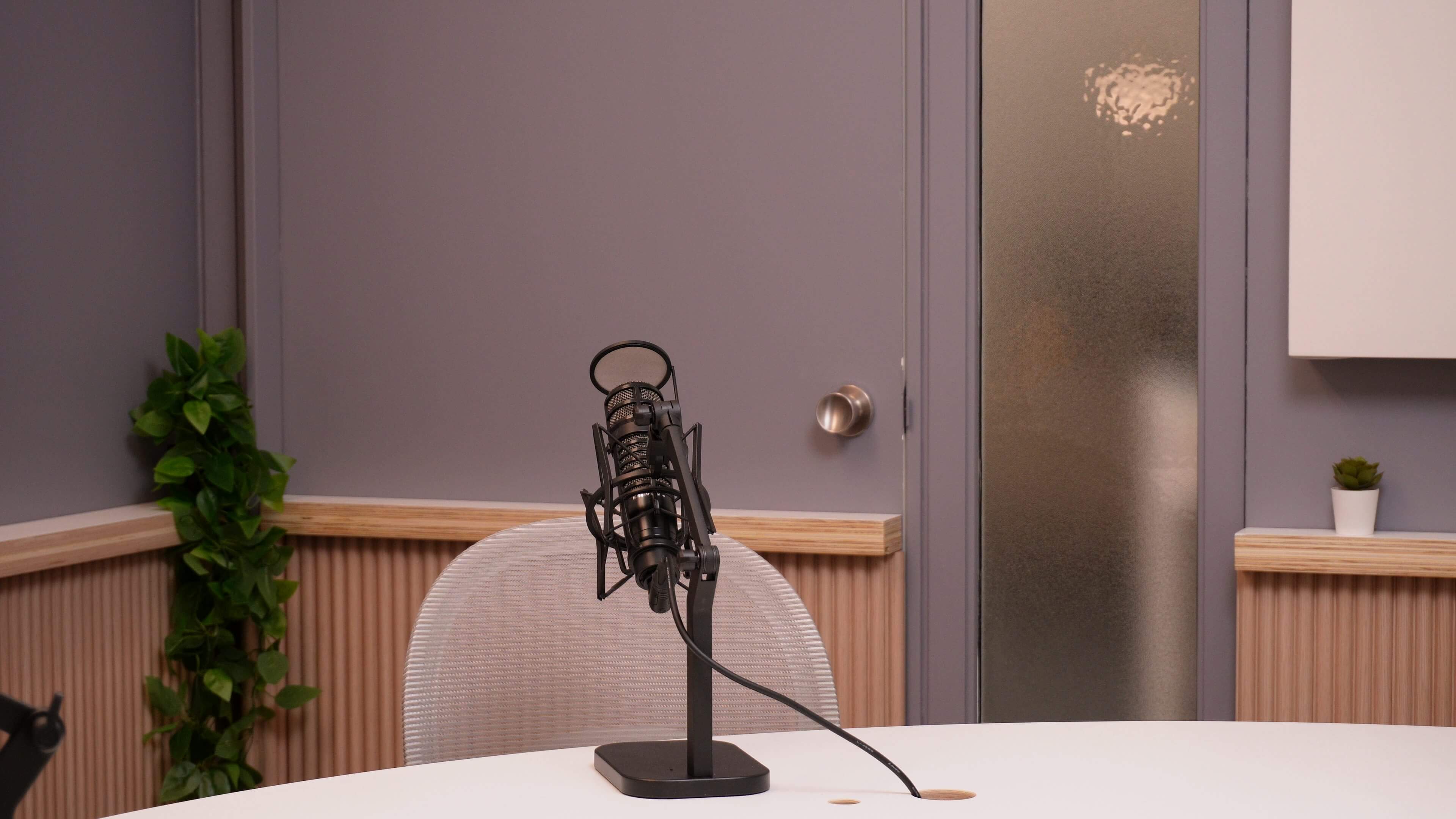 A microphone stands on a table in a recording studio next to a frosted glass door.
