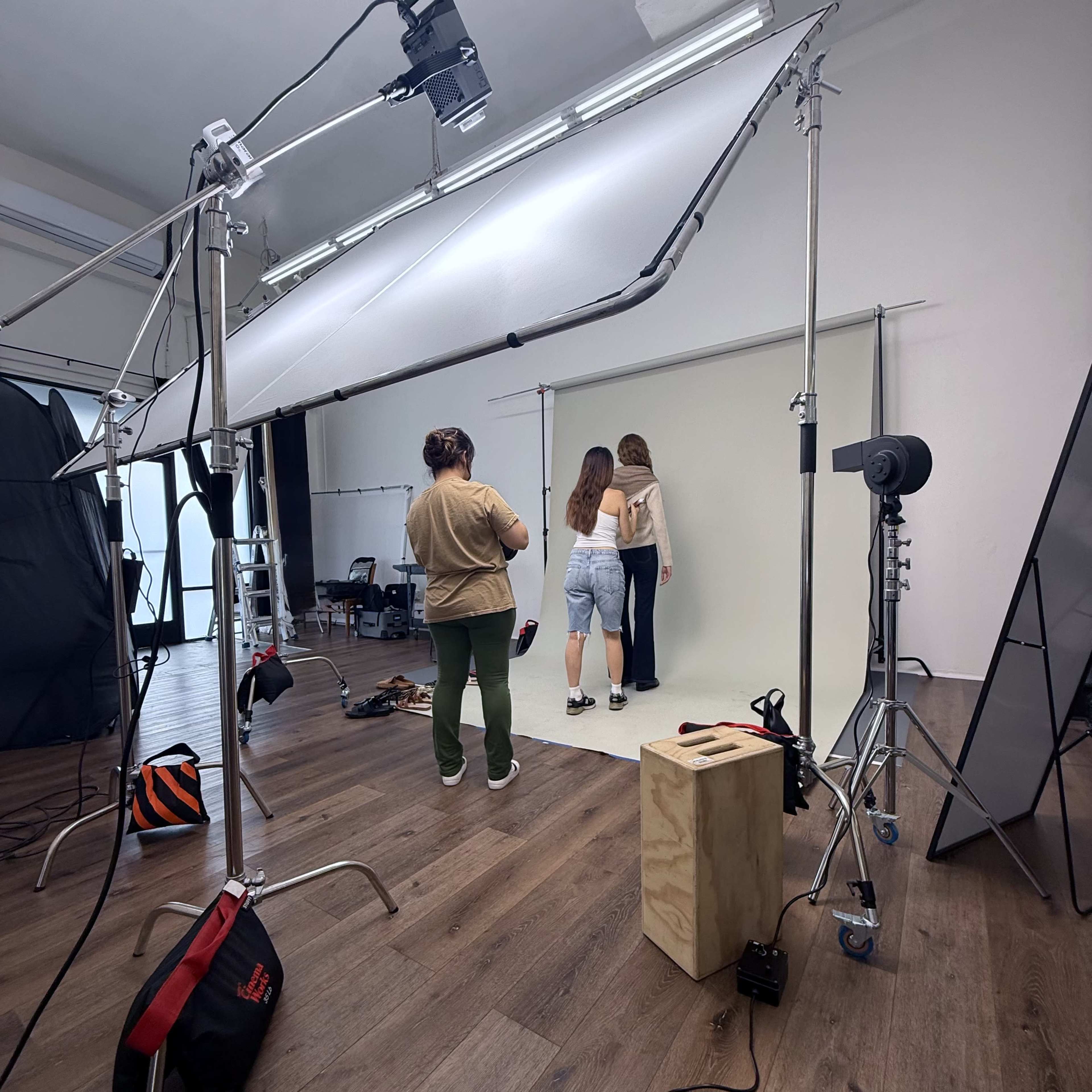 Two models pose against a neutral backdrop in a photography studio, while a photographer adjusts equipment nearby.