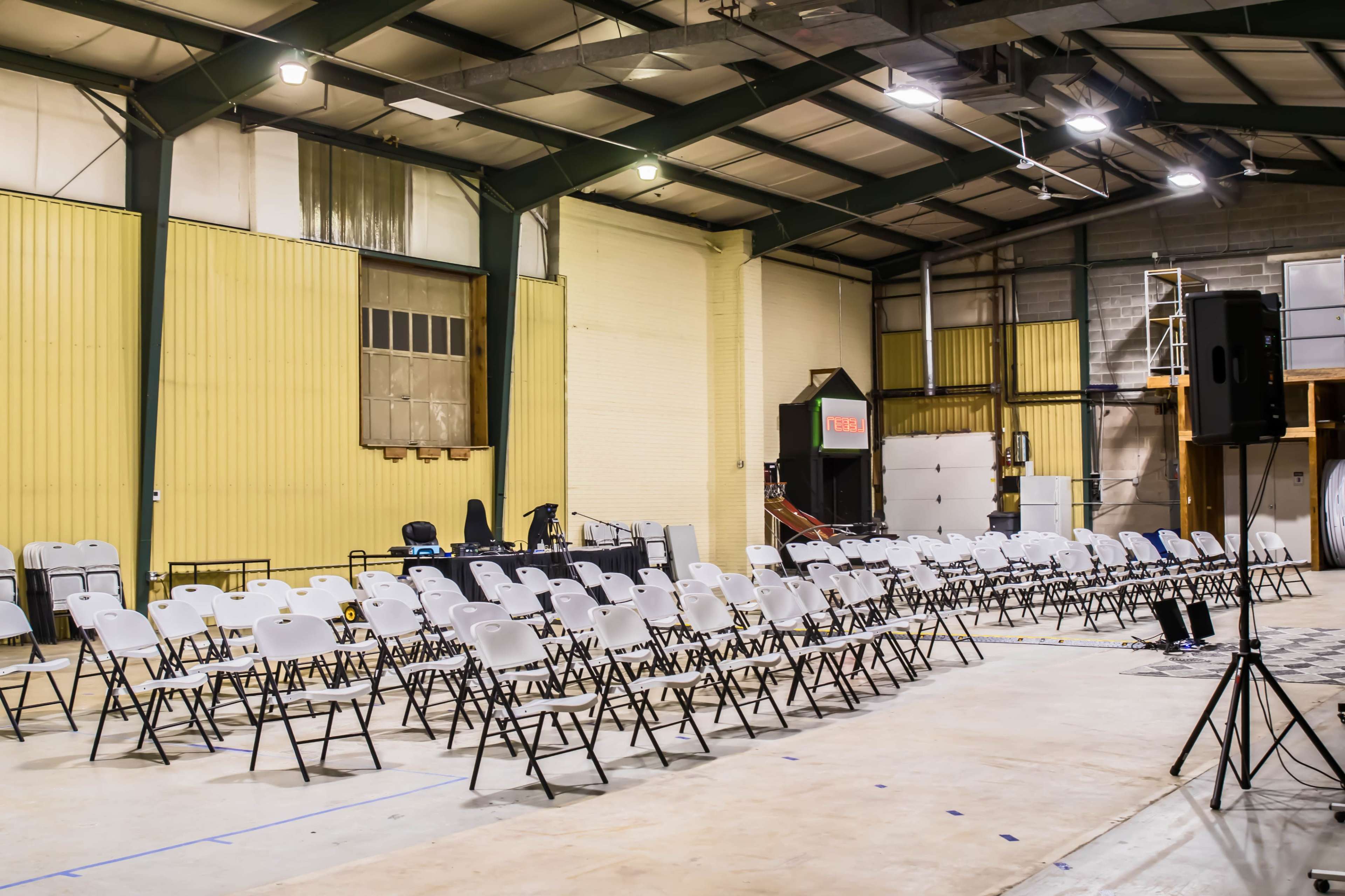 A large indoor space with rows of white folding chairs arranged neatly on a concrete floor.