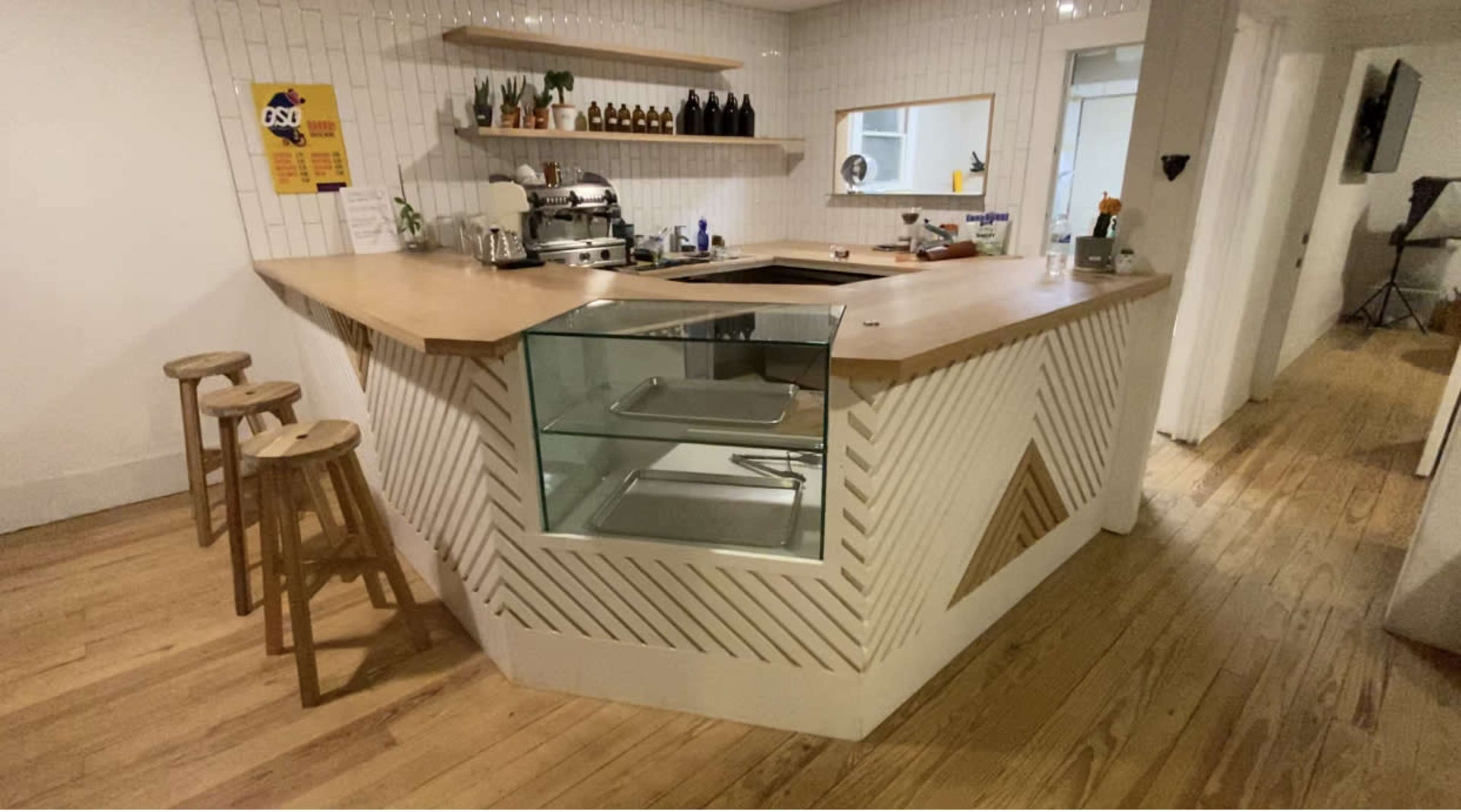 A modern kitchen with a wooden counter, a glass display section, and several shelves featuring plants and condiments.