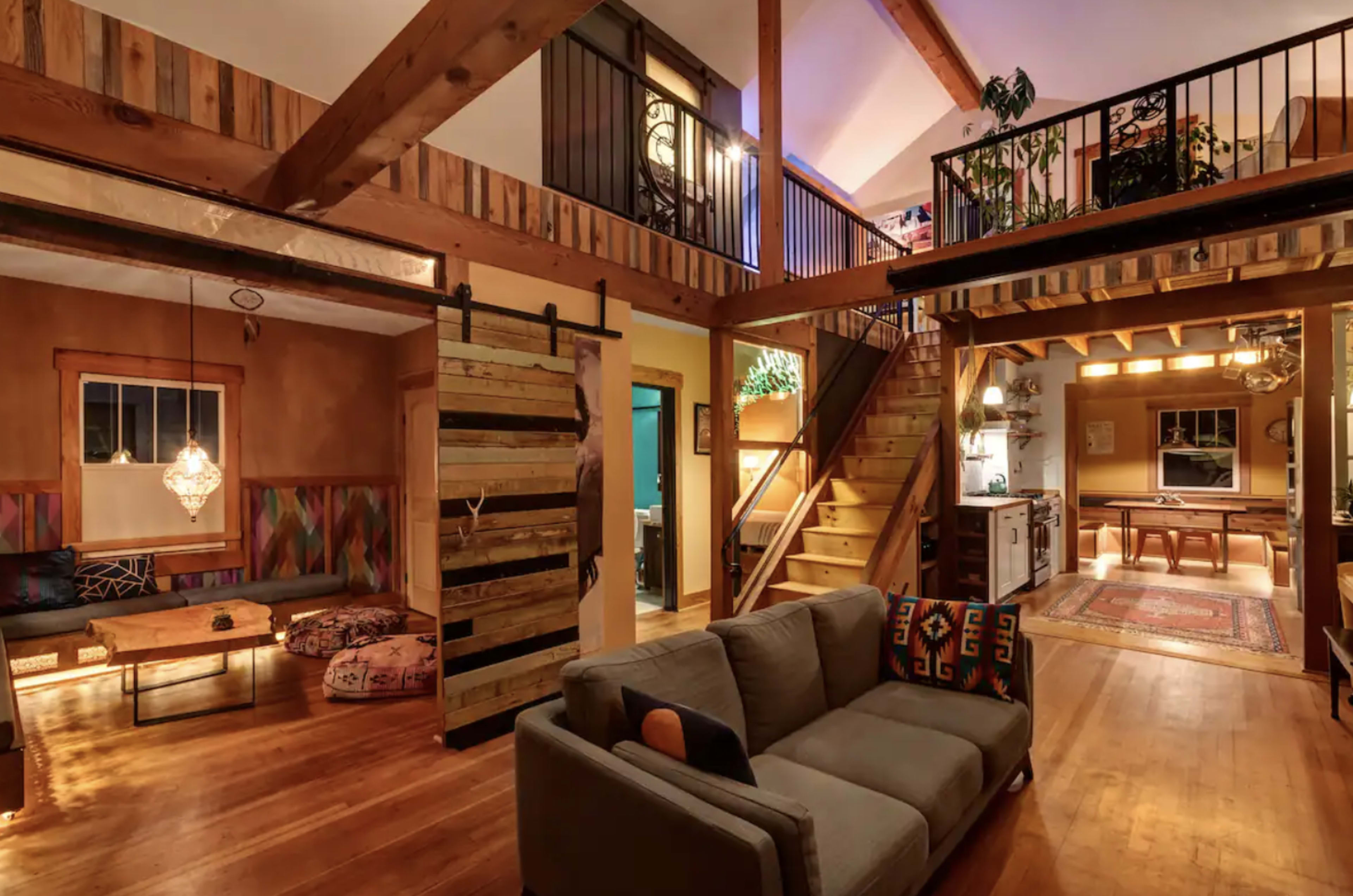 A spacious living area with wooden beams, a staircase leading to a second floor, and a cozy seating arrangement on one side.