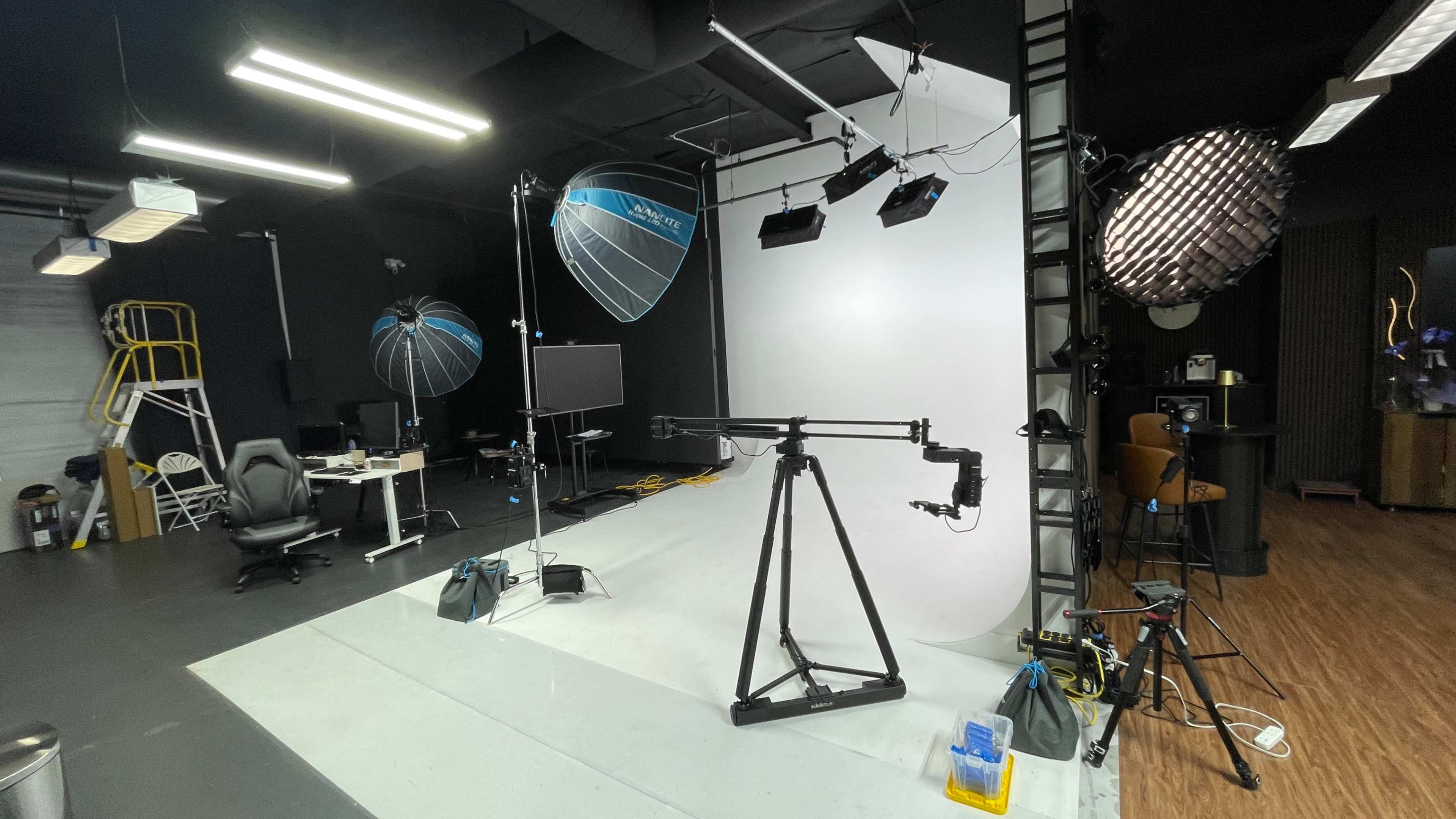 The image shows a photography studio equipped with various lighting setups, a backdrop, a camera rig, and a few pieces of furniture.