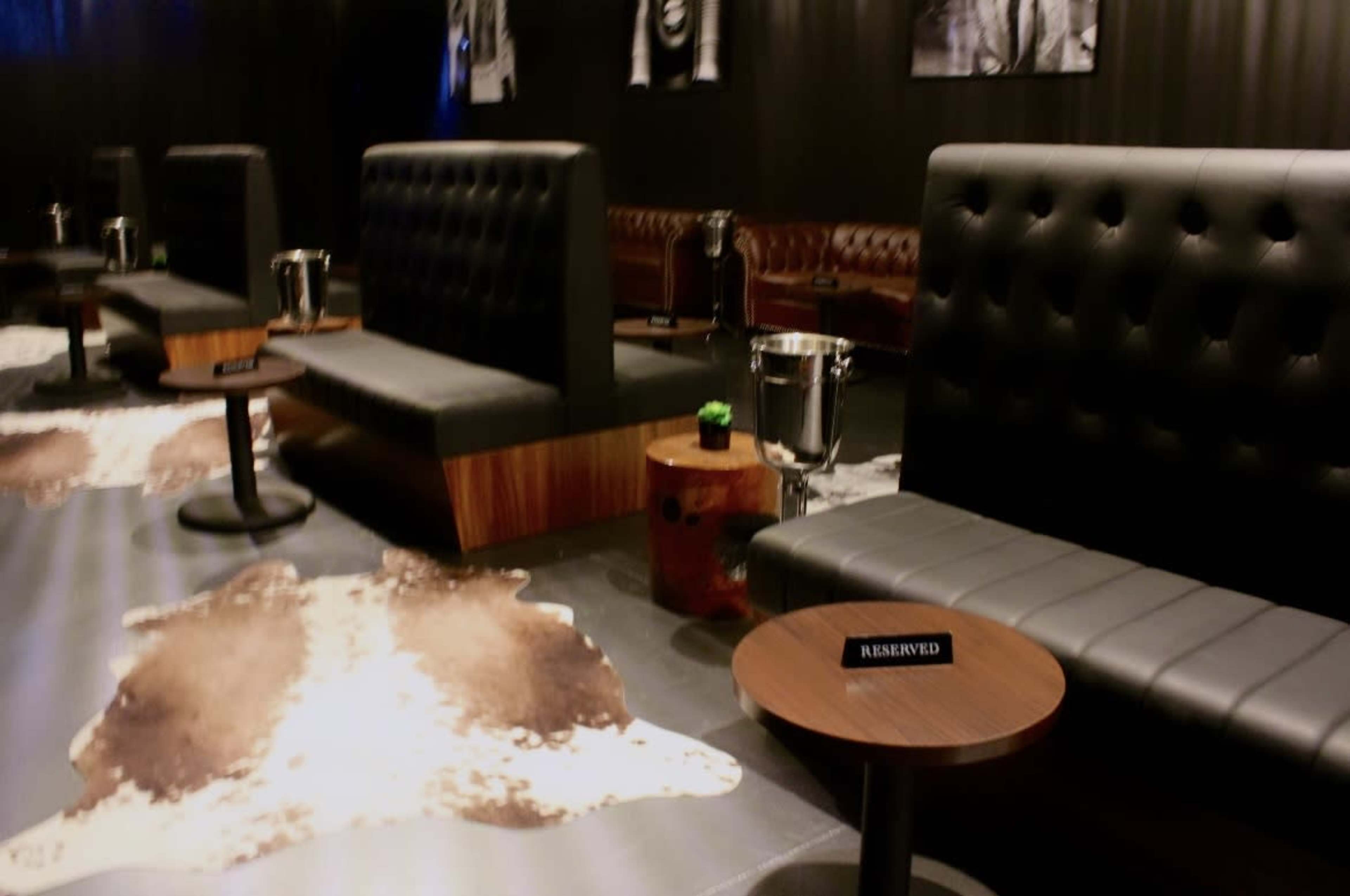 A stylish lounge area featuring brown leather seating, small tables with "RESERVED" signs, and decorative rugs on a polished floor.