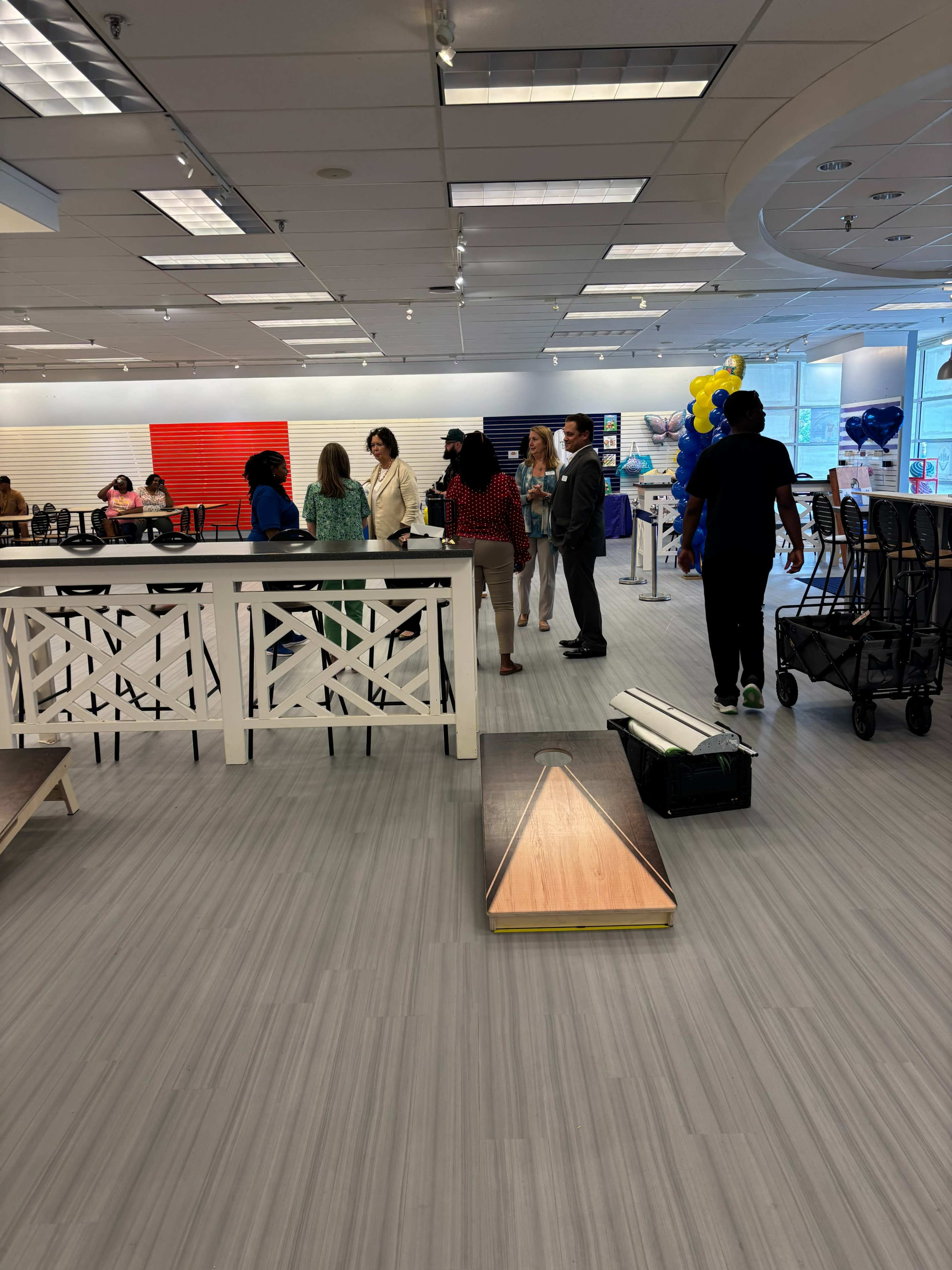 A group of people is gathered in a brightly lit retail space with a large white counter and colorful wall decorations.