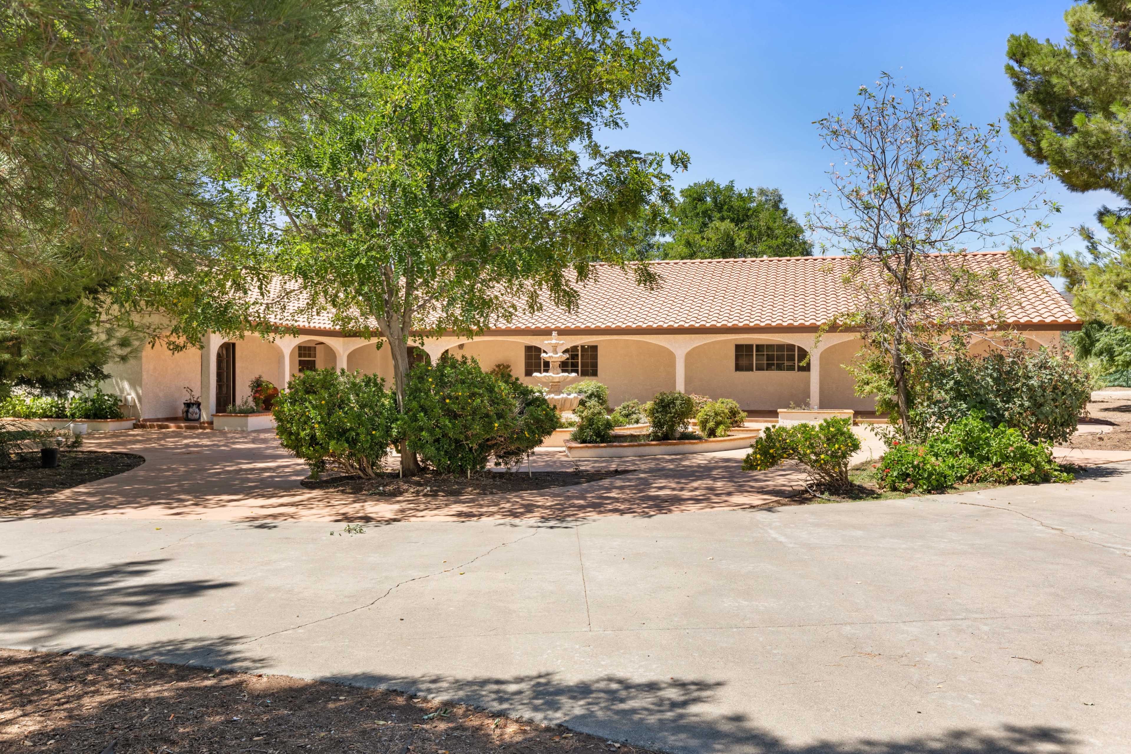 A single-story house with a tiled roof is surrounded by greenery and features a spacious driveway.