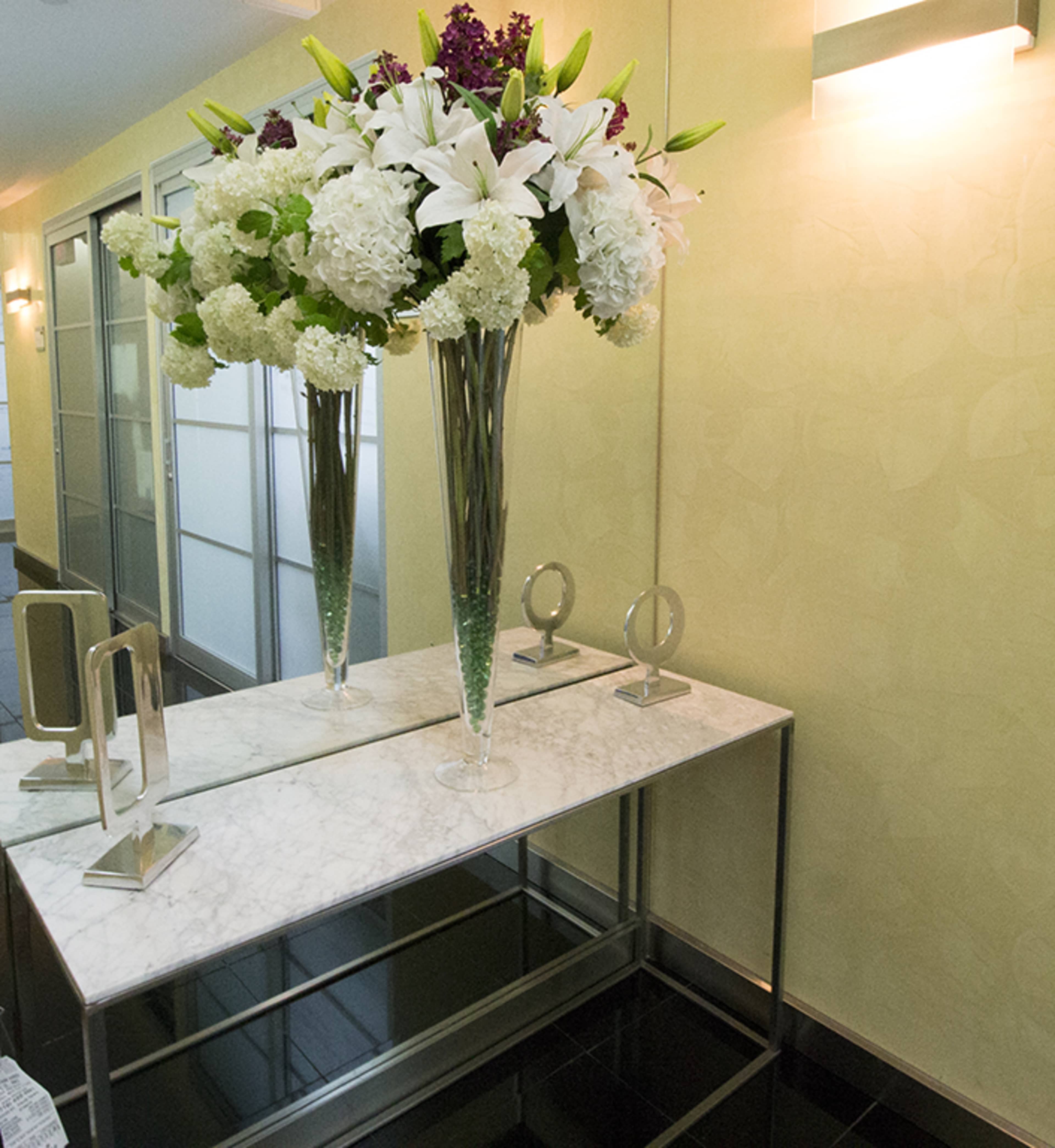 A modern entryway features a marble table adorned with large flower arrangements and two decorative mirrors.