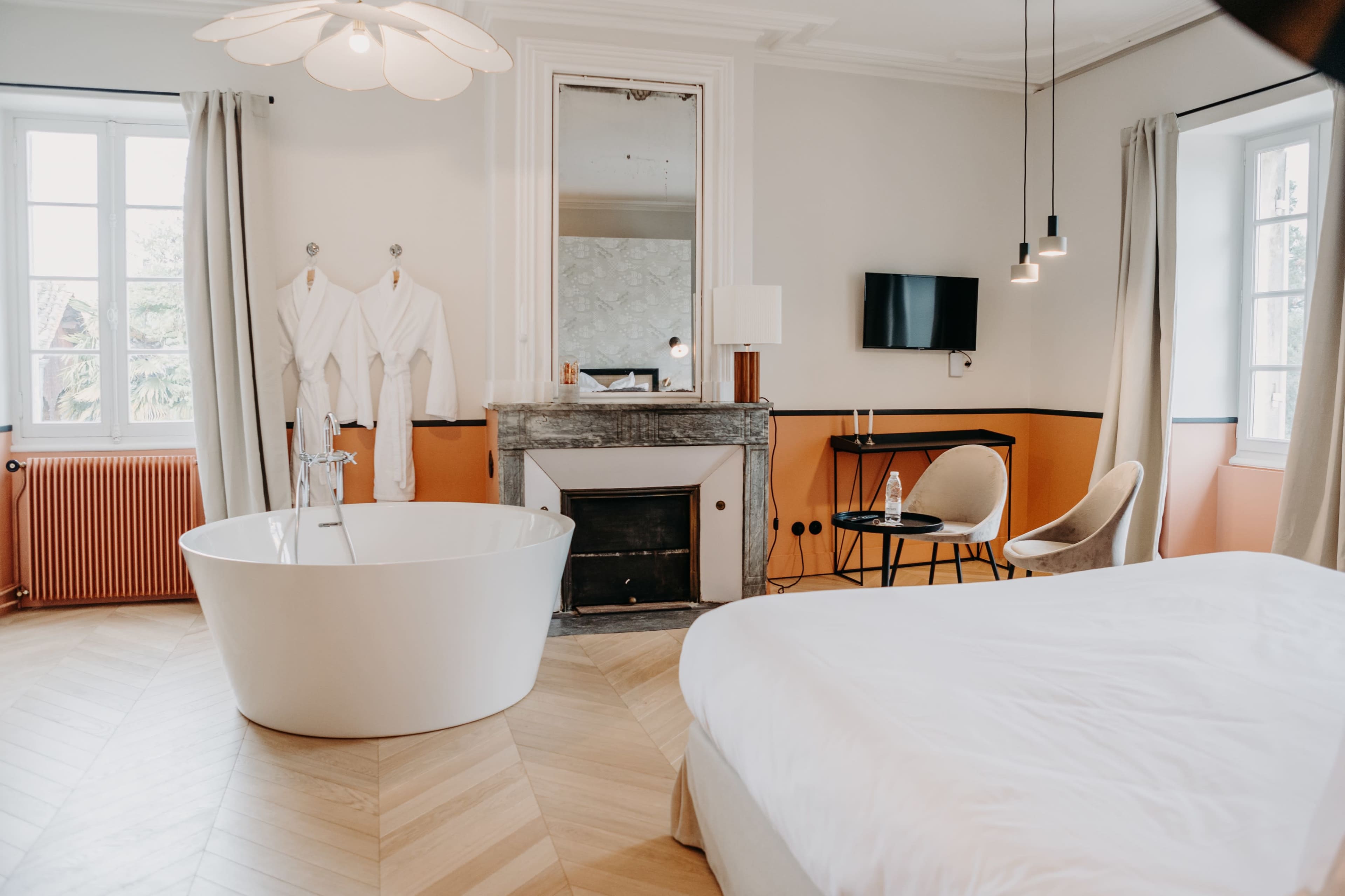 A modern hotel room featuring a freestanding bathtub, a large bed, and a fireplace with a wall-mounted television.