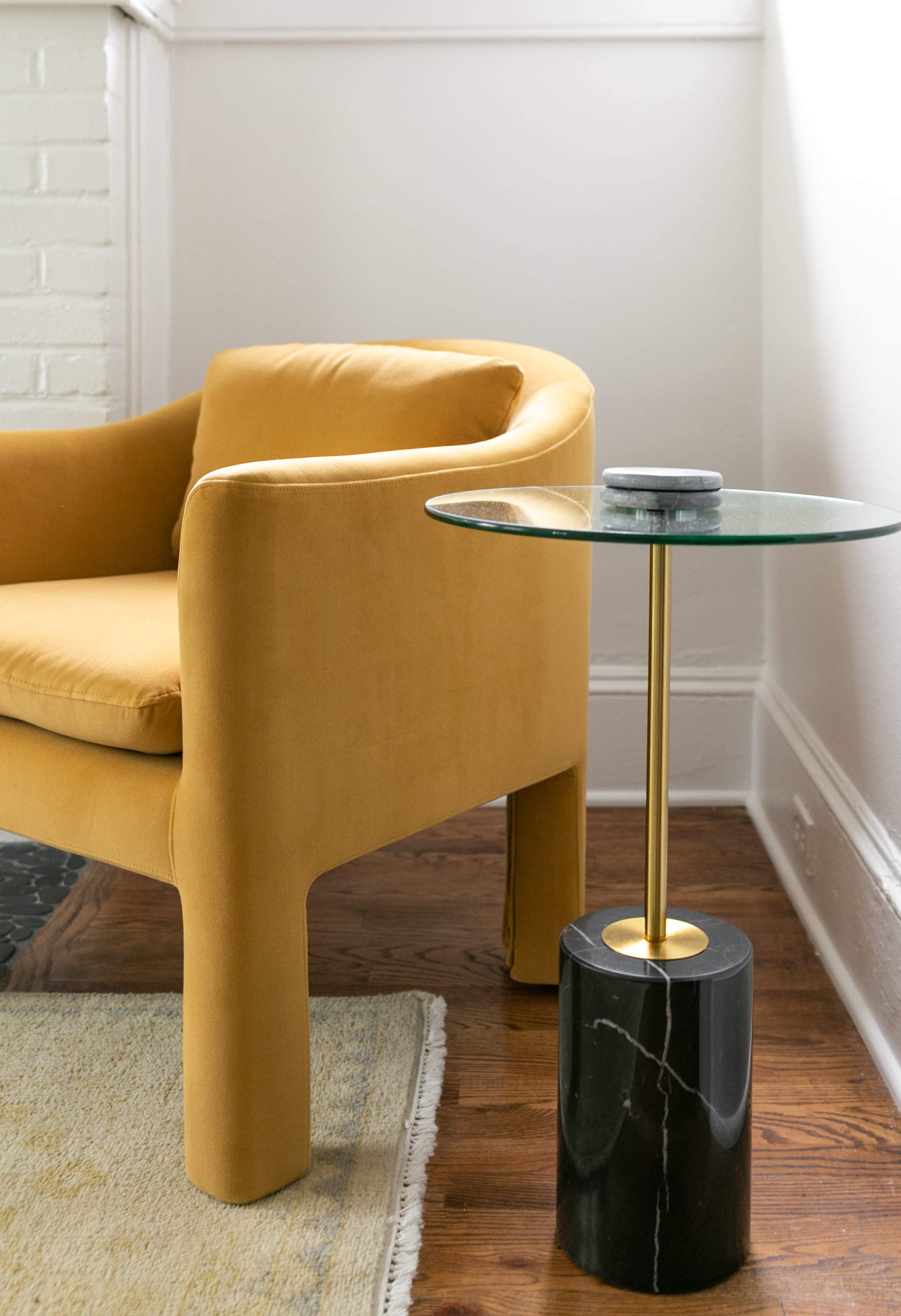 A yellow upholstered chair is positioned next to a black marble side table with a glass top.
