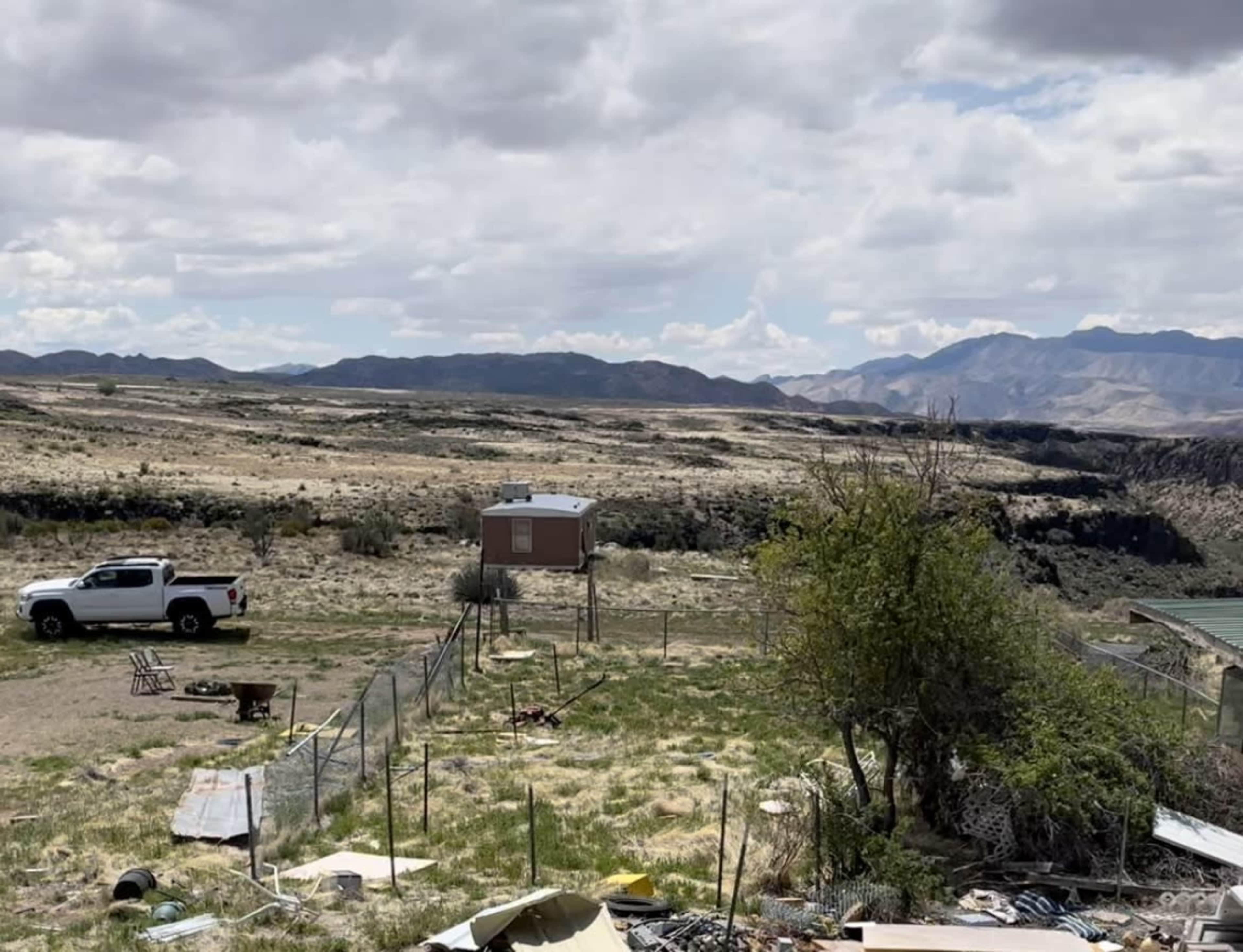 The image shows a barren landscape with a white pickup truck parked near a small structure, surrounded by scattered debris and fencing.