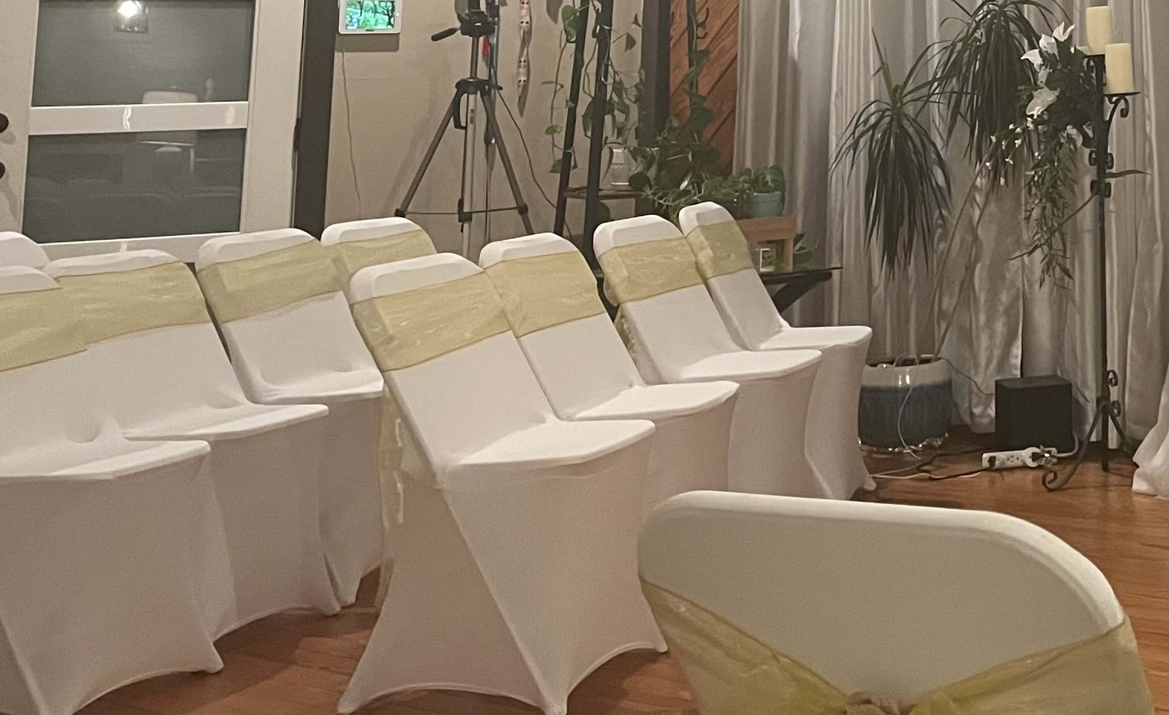 The image shows a decorated indoor venue with rows of white chairs draped in yellow sashes.