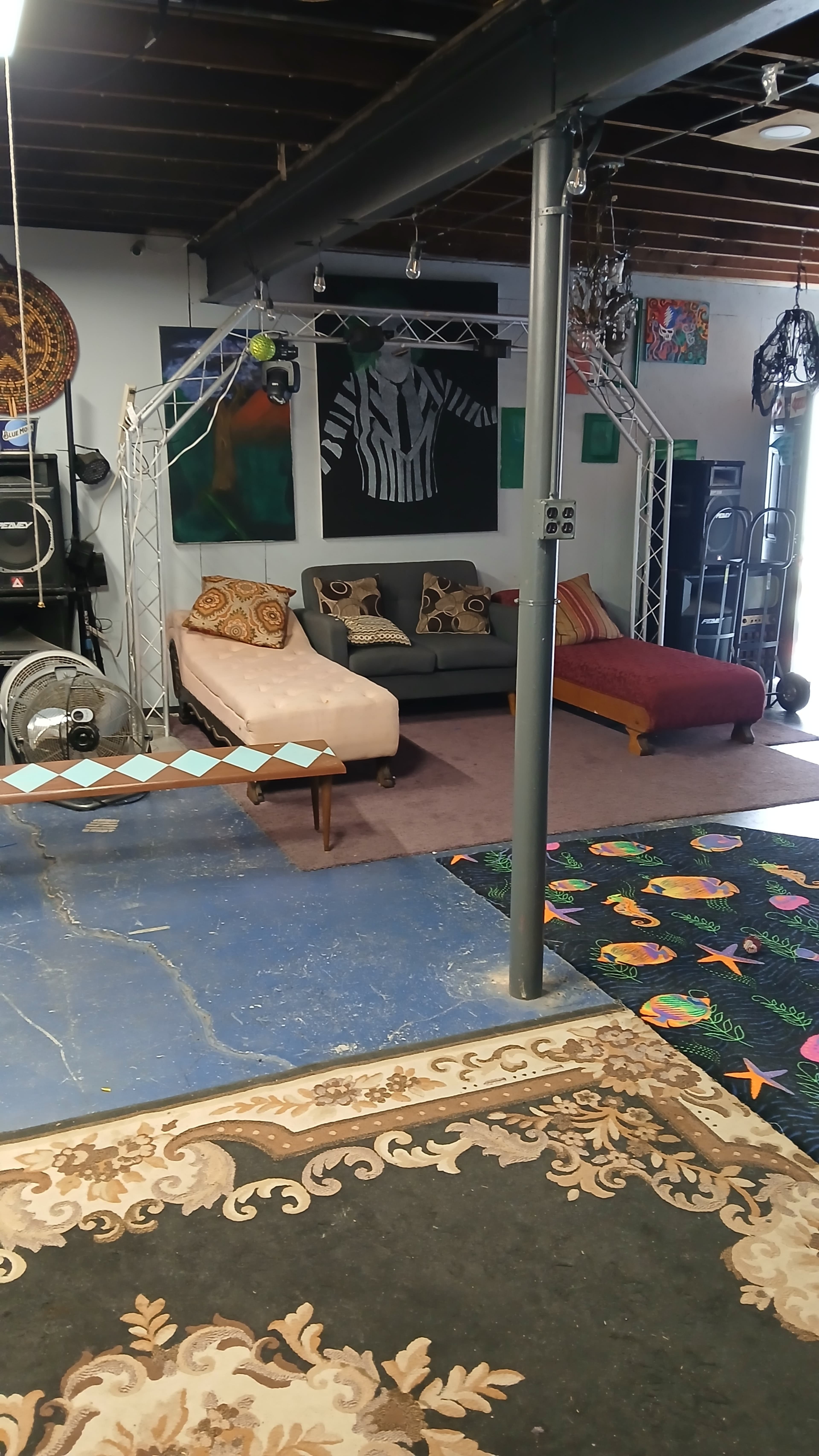 The image shows a spacious room with two sofas, colorful rugs on the floor, and artwork displayed on the walls.