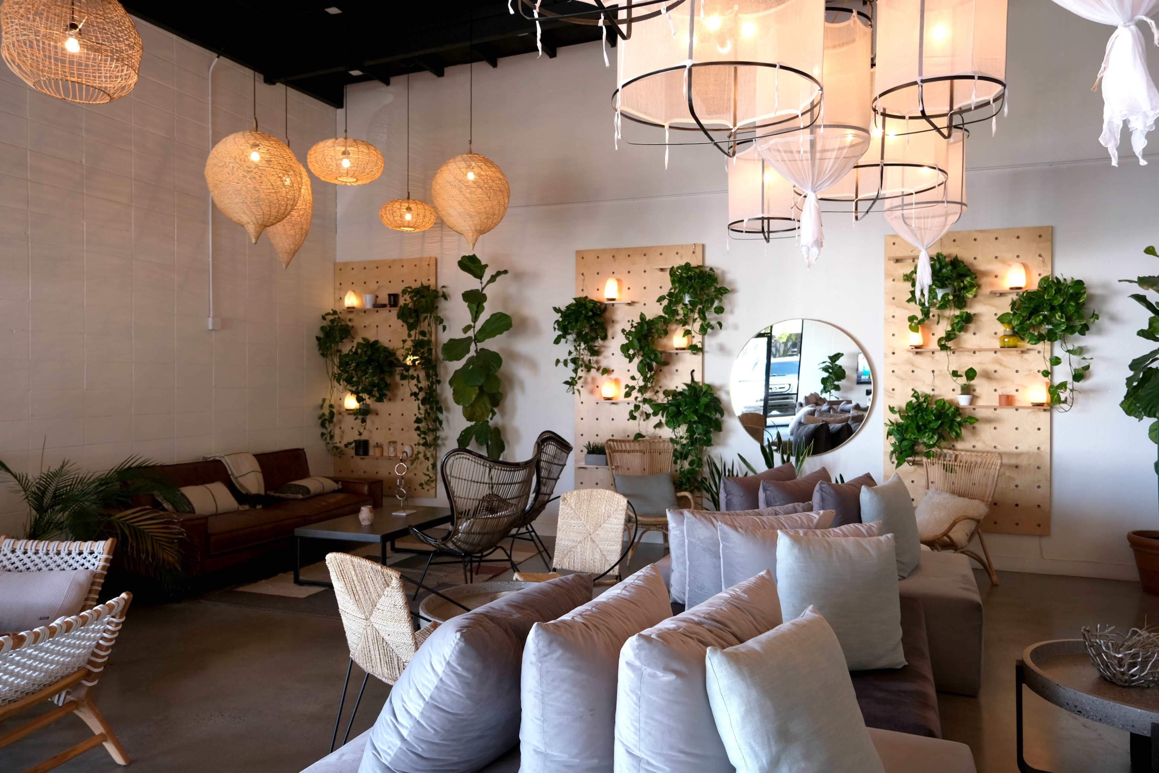 The image depicts a modern interior space featuring comfortable seating, decorative plants on the walls, and ambient lighting with woven pendant fixtures.