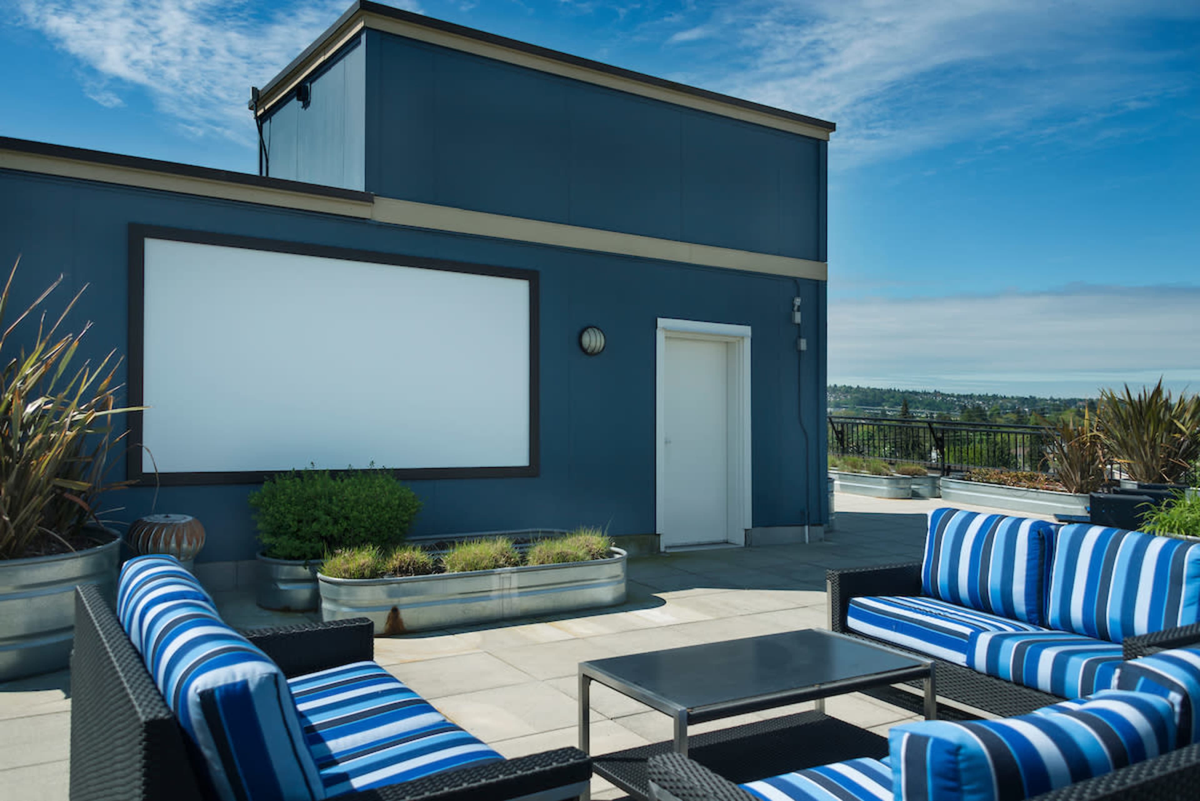 A rooftop patio features striped seating, a coffee table, and a blank screen mounted on the wall.