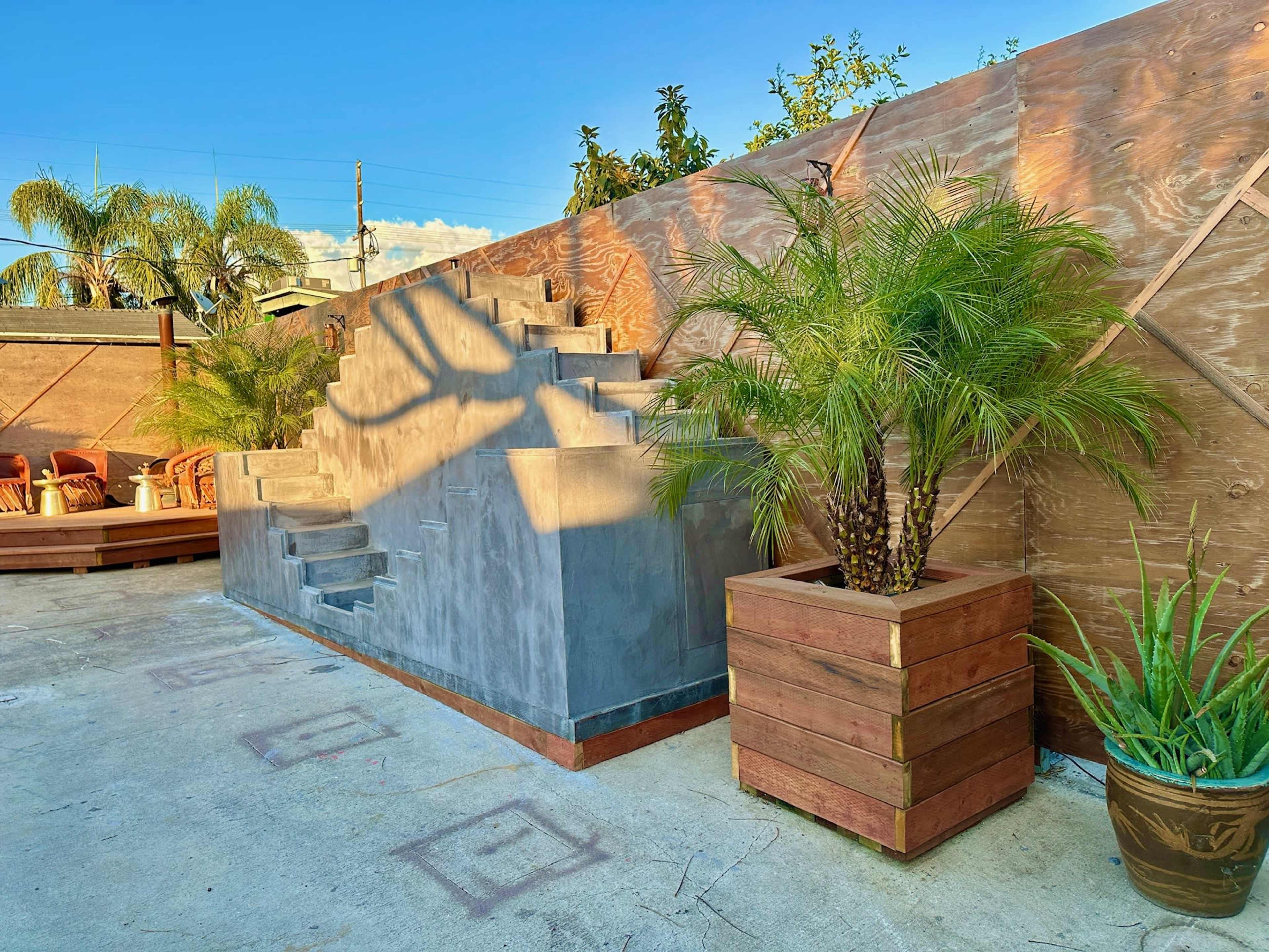 A set of concrete stairs leading up to a raised platform, surrounded by palm trees and wooden fencing.