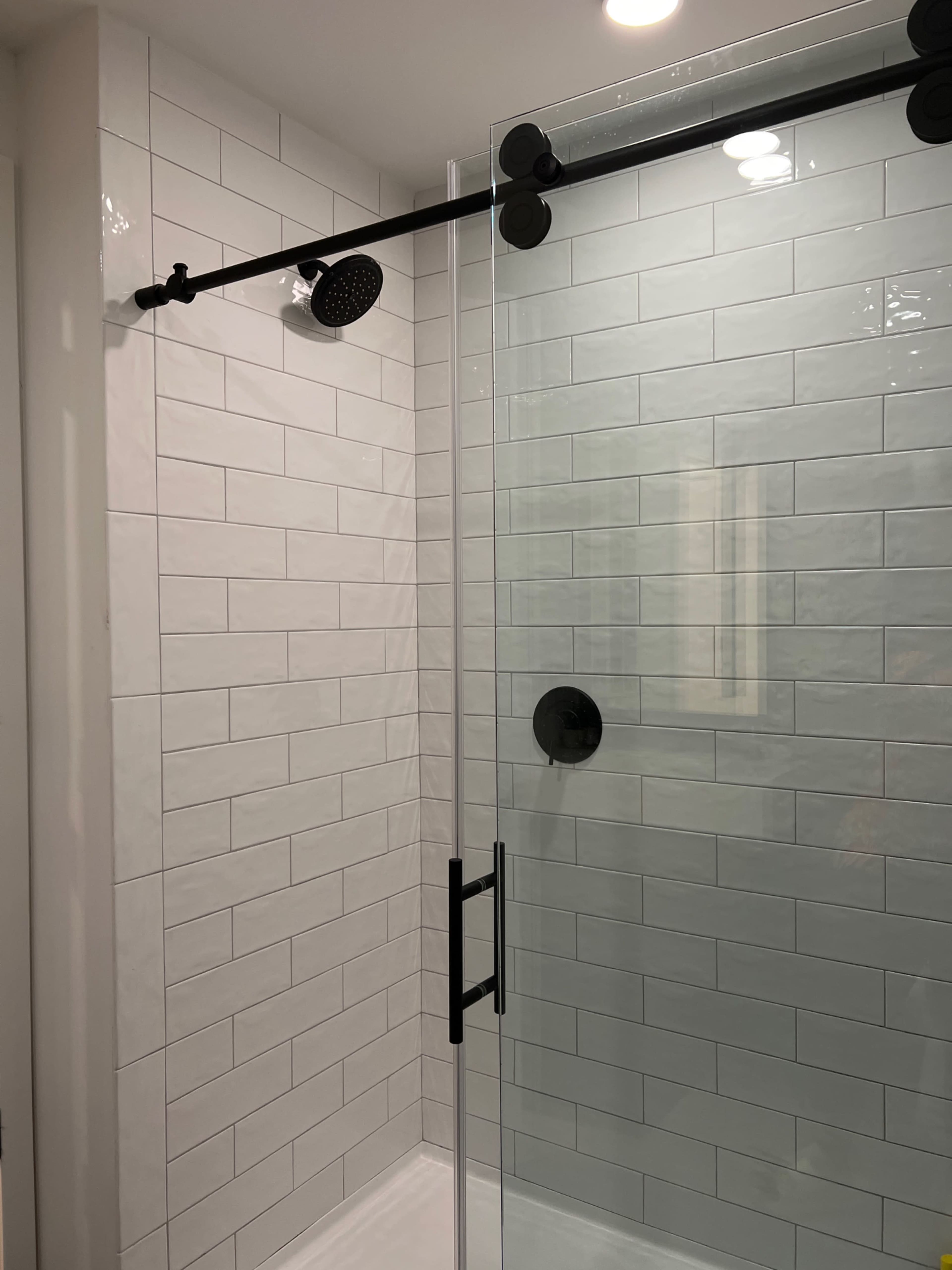 A modern shower with a glass door, black fixtures, and white tiled walls.