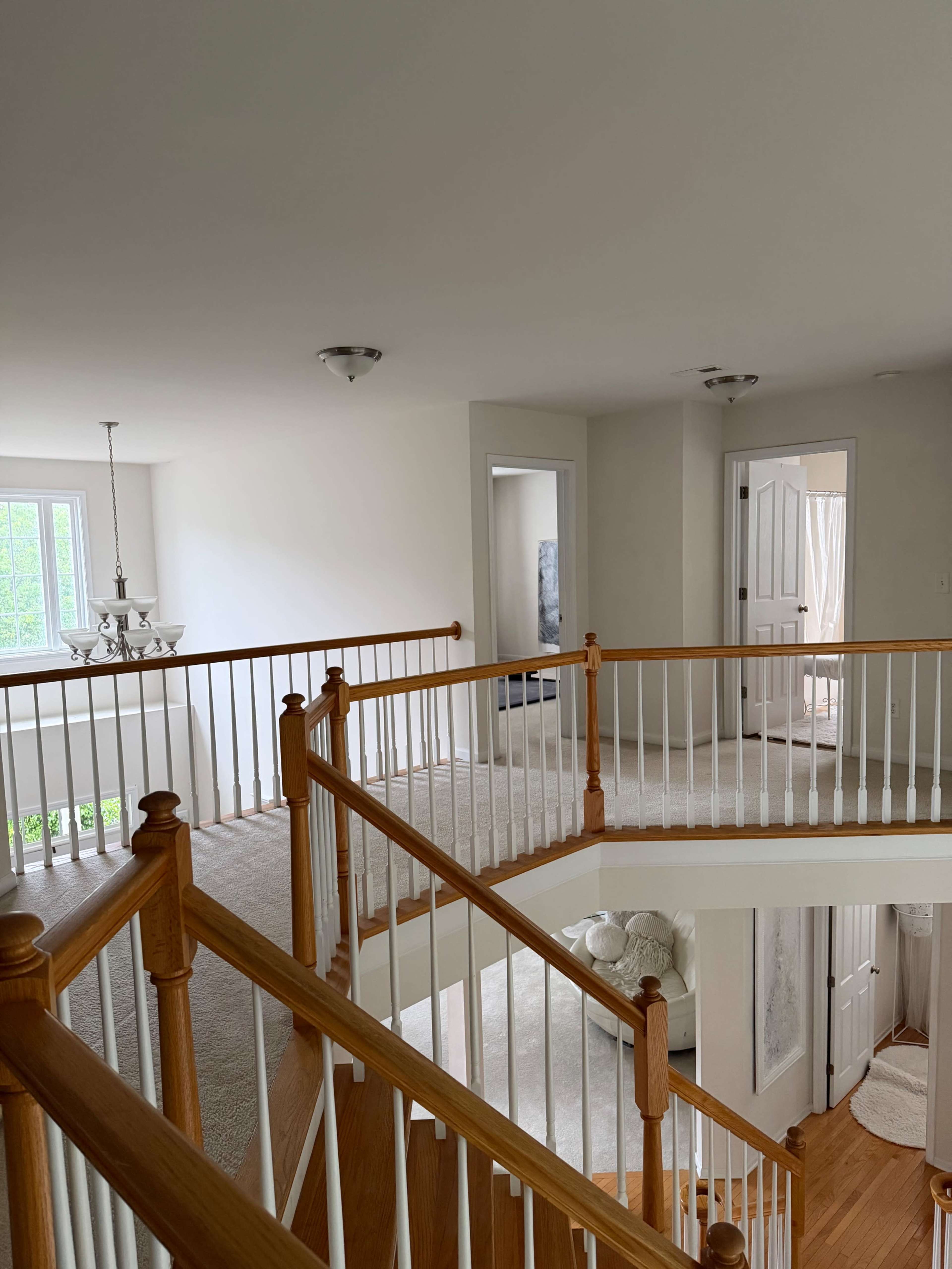 The image shows a well-lit interior of a house featuring a staircase with wooden railings, leading to a landing area that opens to multiple doorways.