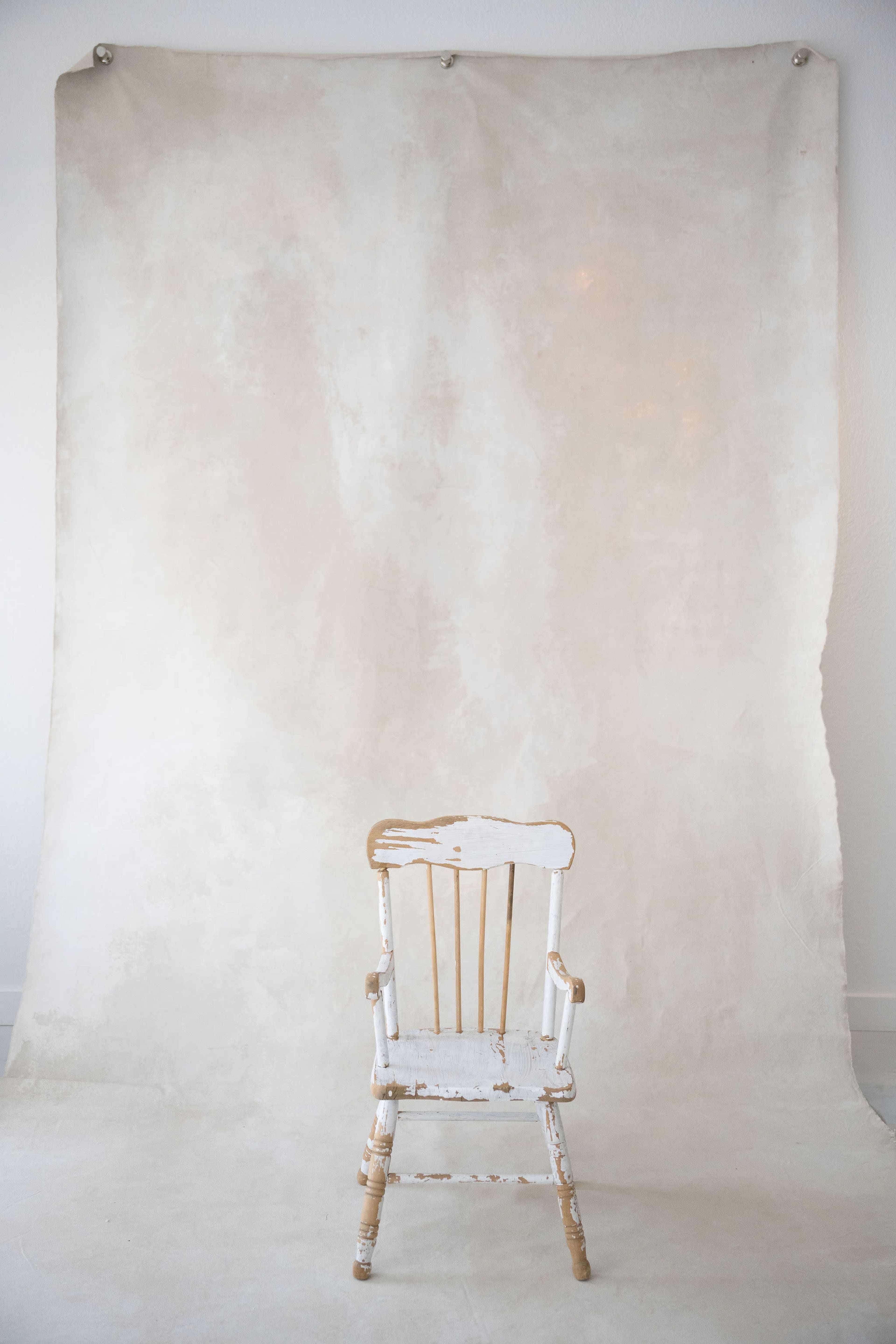 A weathered white chair is positioned in front of a plain, light-colored backdrop.