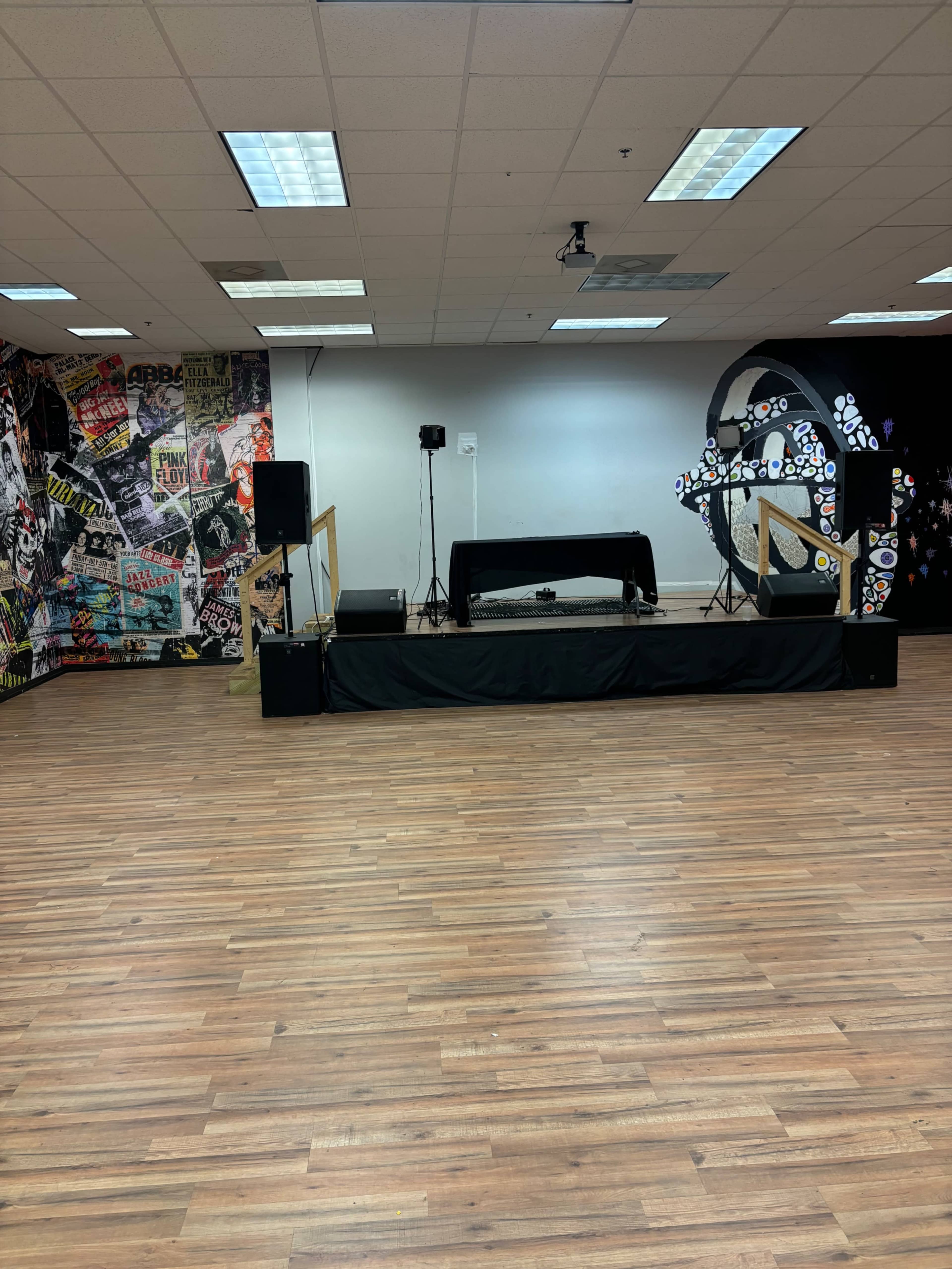 The image shows a spacious performance area with a raised platform, surrounded by a wall decorated with colorful music-themed posters.