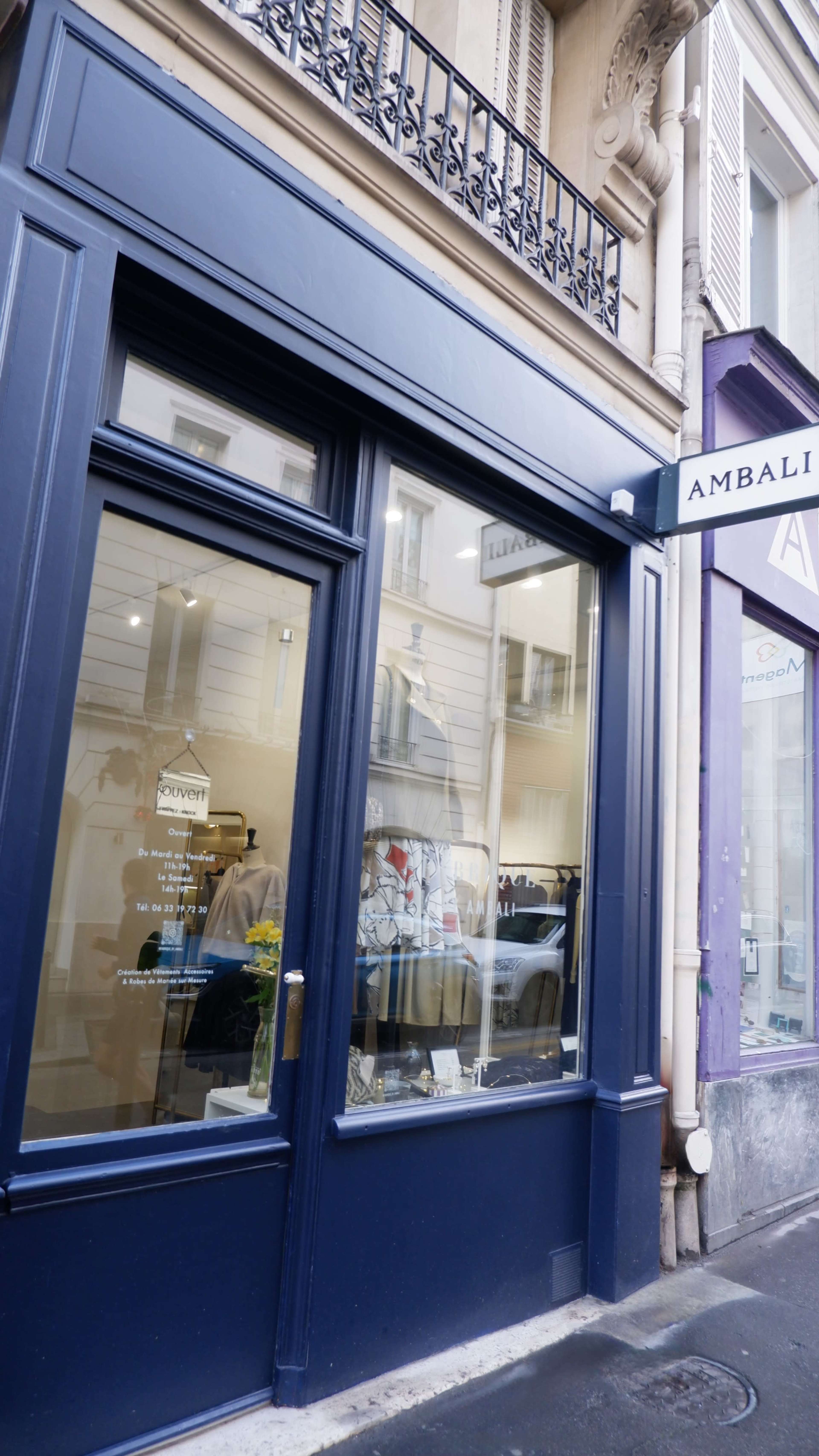 A storefront with large glass windows displaying clothing and signage, located on a narrow street in Paris.