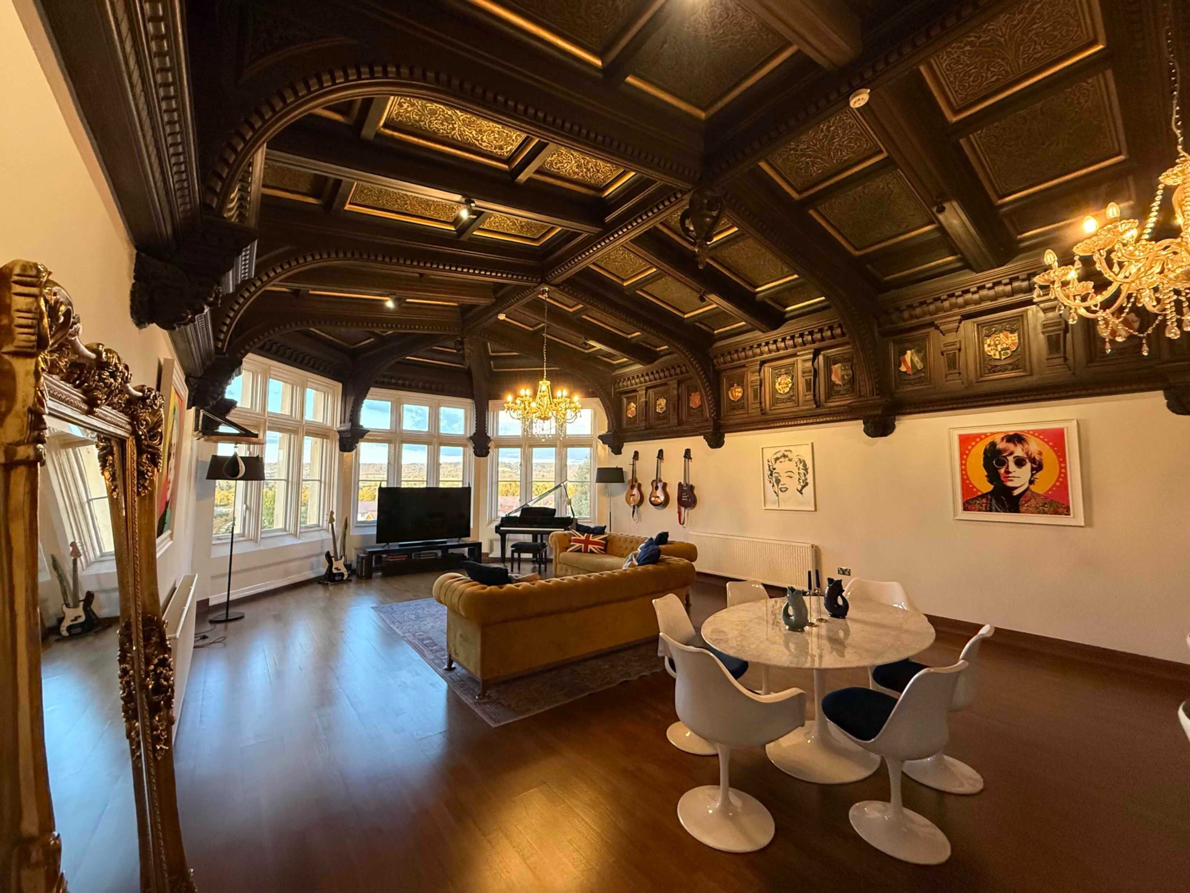 The image shows a spacious, elegantly designed living room with a coffered ceiling, large windows, and a mix of modern and classical furnishings.
